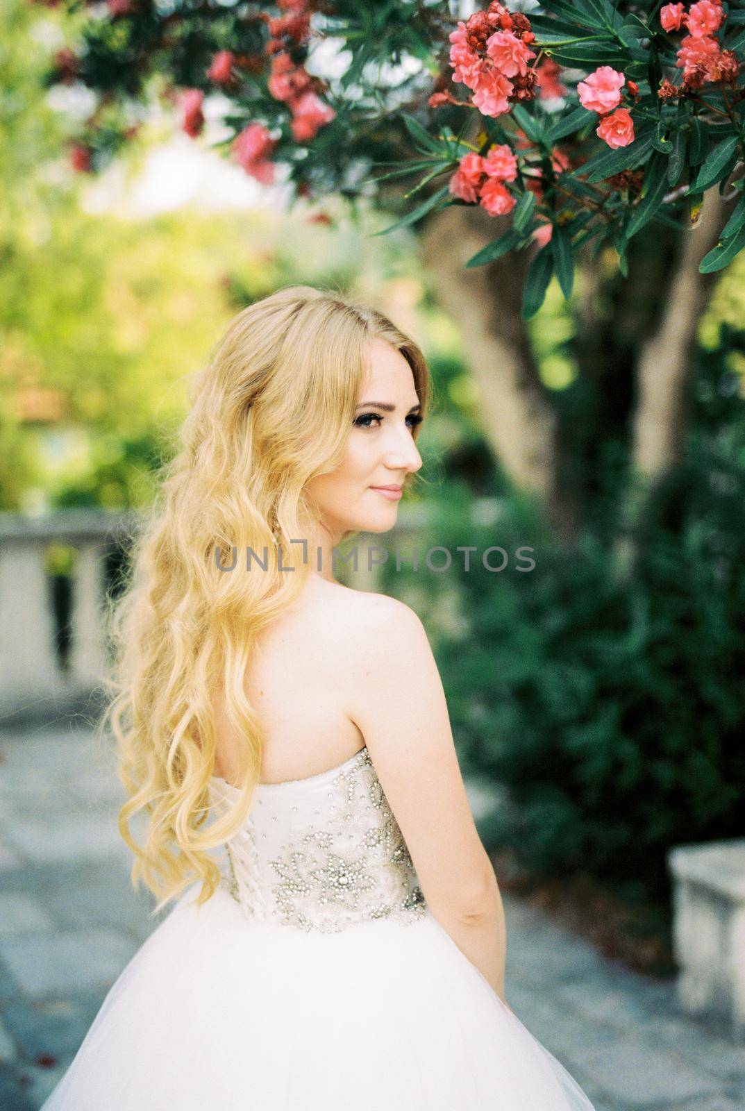 Bride stands next to a tree blooming with pink flowers. High quality photo