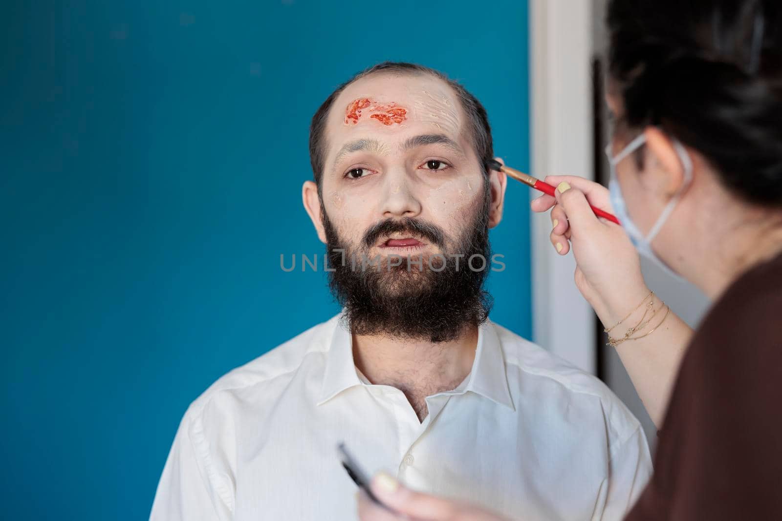 Makeup artist using special effects to create zombie costume and scary dramatic corpse look. Man looking deceased and infected after having bloody scars and monster face, creepy design.