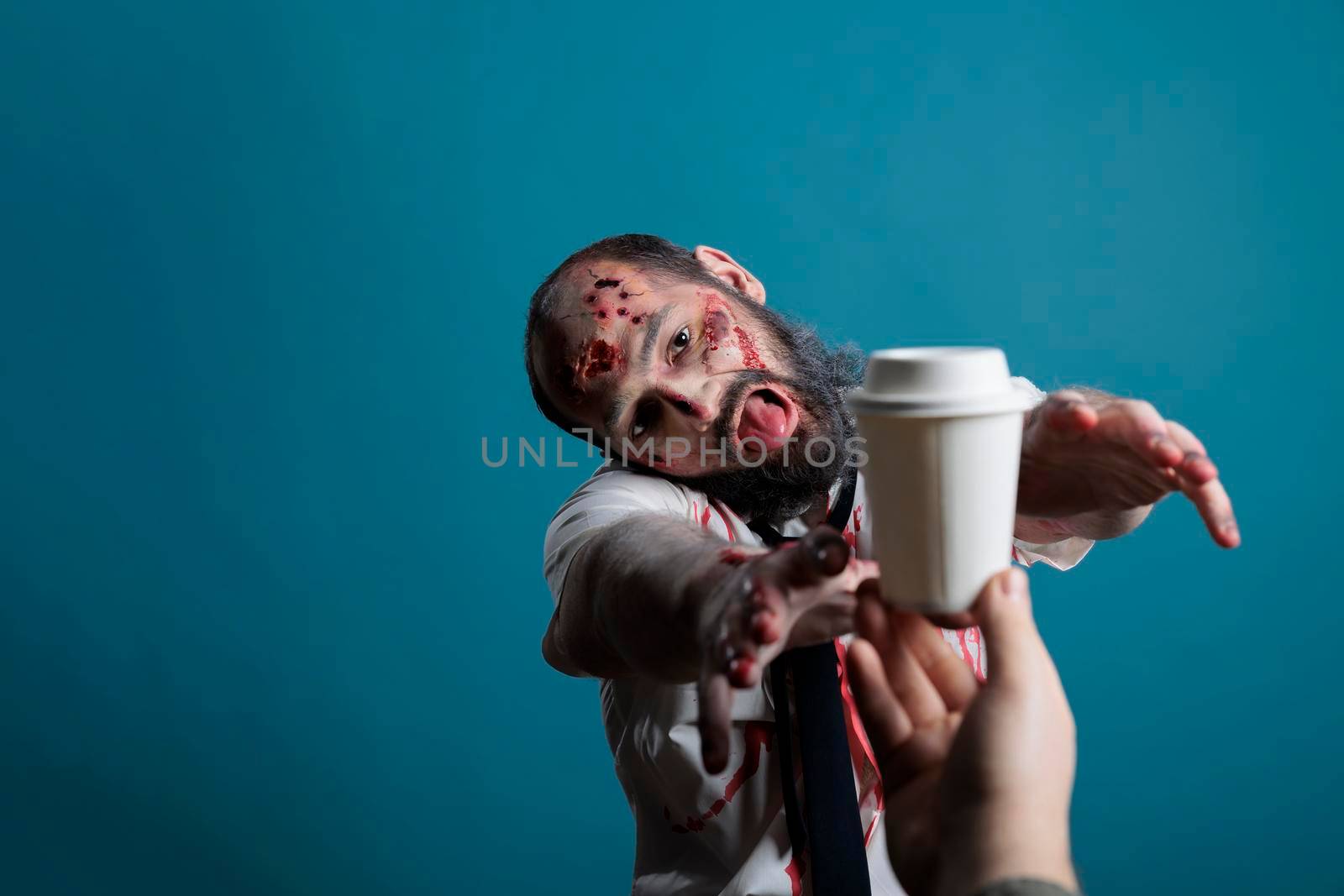 Aggressive halloween corpse wishing to drink coffee cup in studio, going after beverage and wanting to eat carbon. Spooky undead scary devil chasing hand with drink, acting dangerous and creepy.