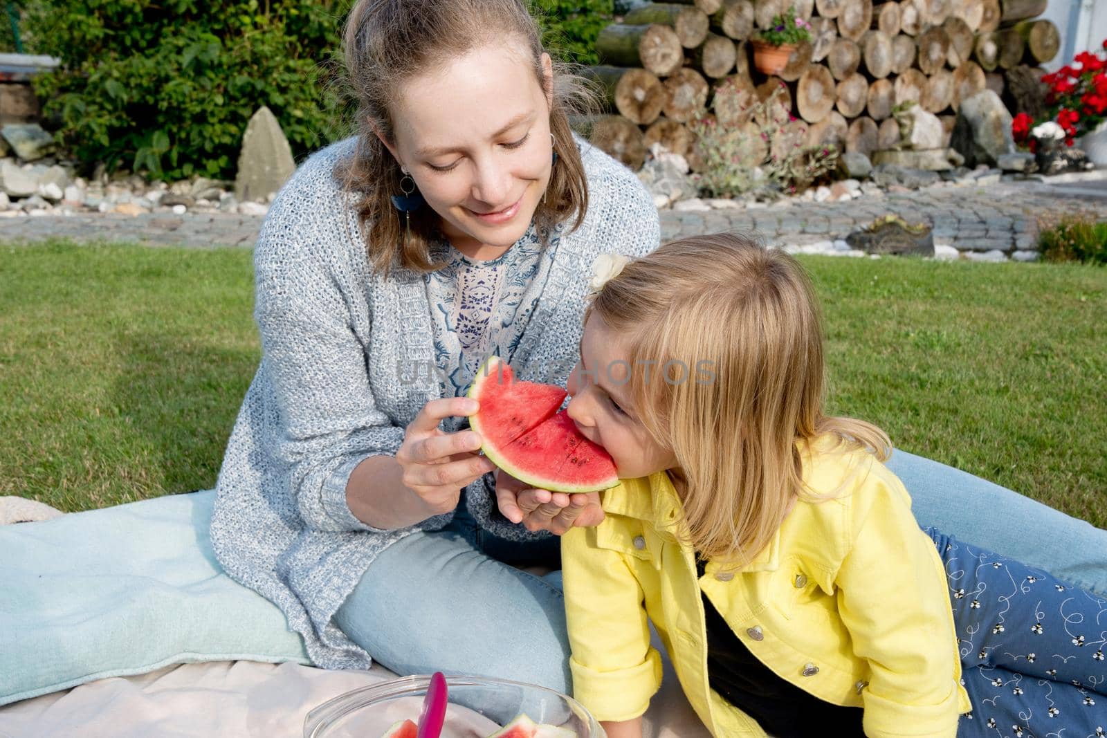 young mother feeds her daughter sweet watermelon, picnic in nature near the house.High quality photo