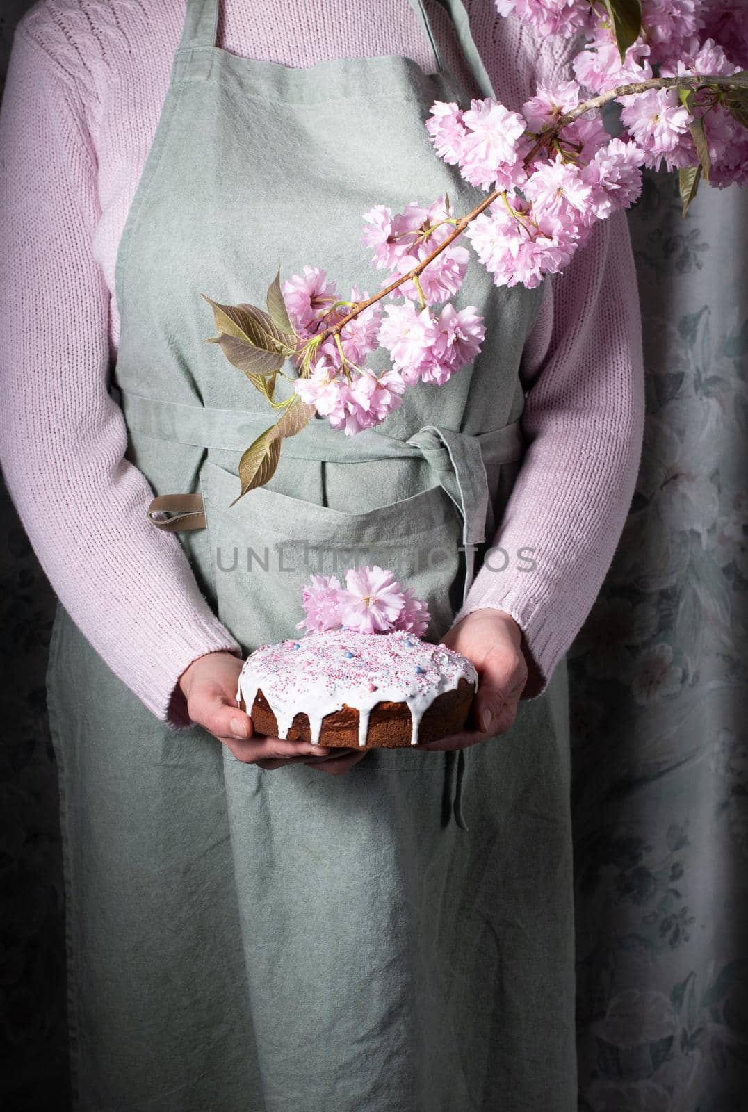 a woman decorates a homemade Easter cake with pink sakura flowers, spring blossom, a bouquet of pink sakura flowers on a table in a decorated spring room, a beautiful still life. High quality photo