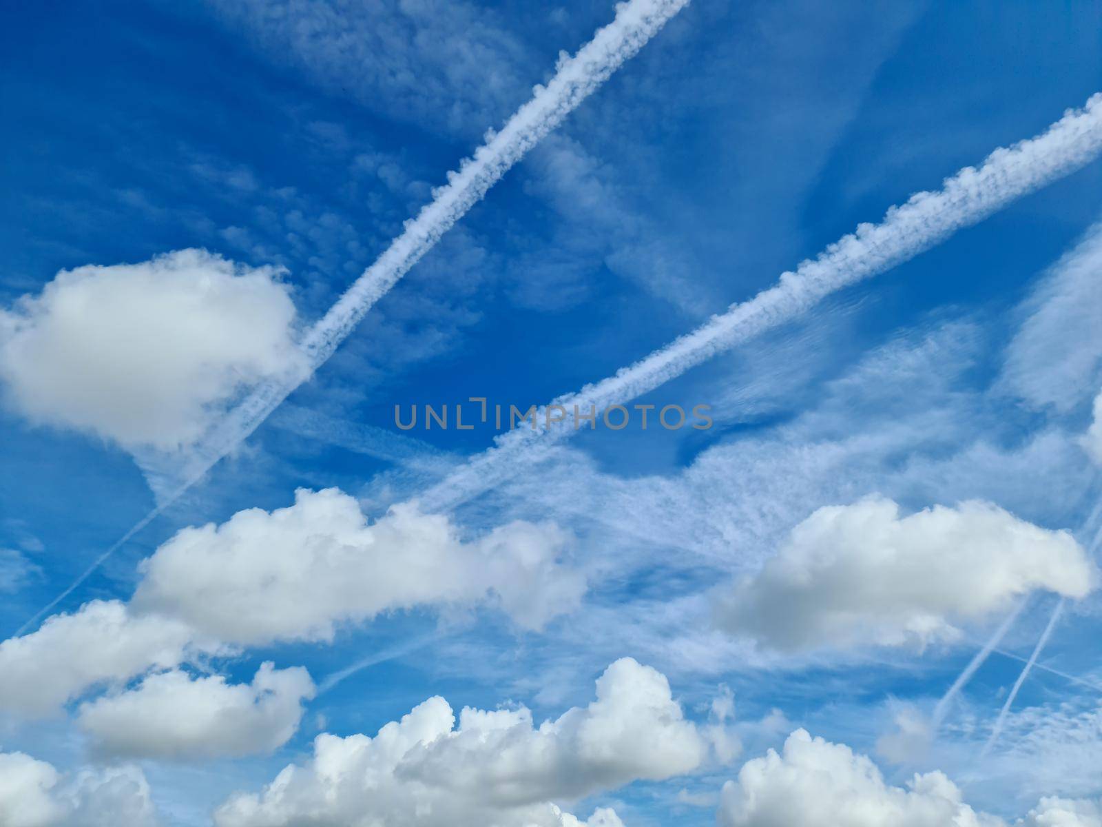 Aircraft condensation contrails in the blue sky inbetween some clouds by MP_foto71