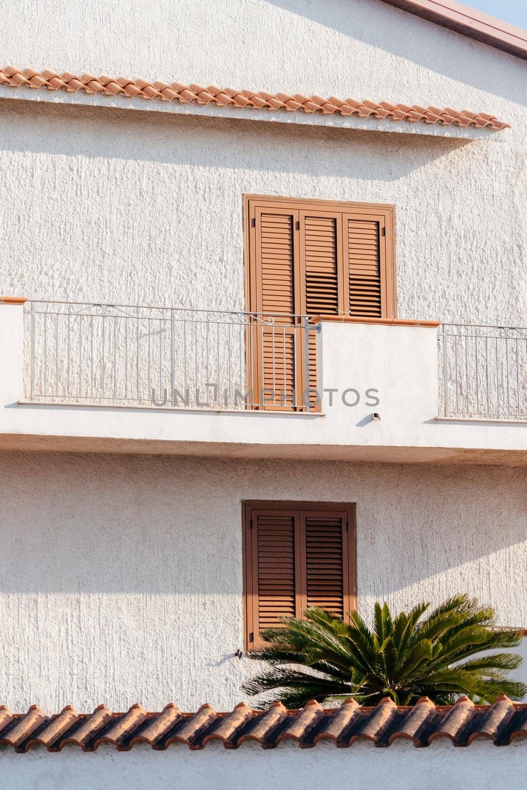 Typical white house facade part in italian city near the sea. Brown windows on white wall. Mediterranean village style architecture.