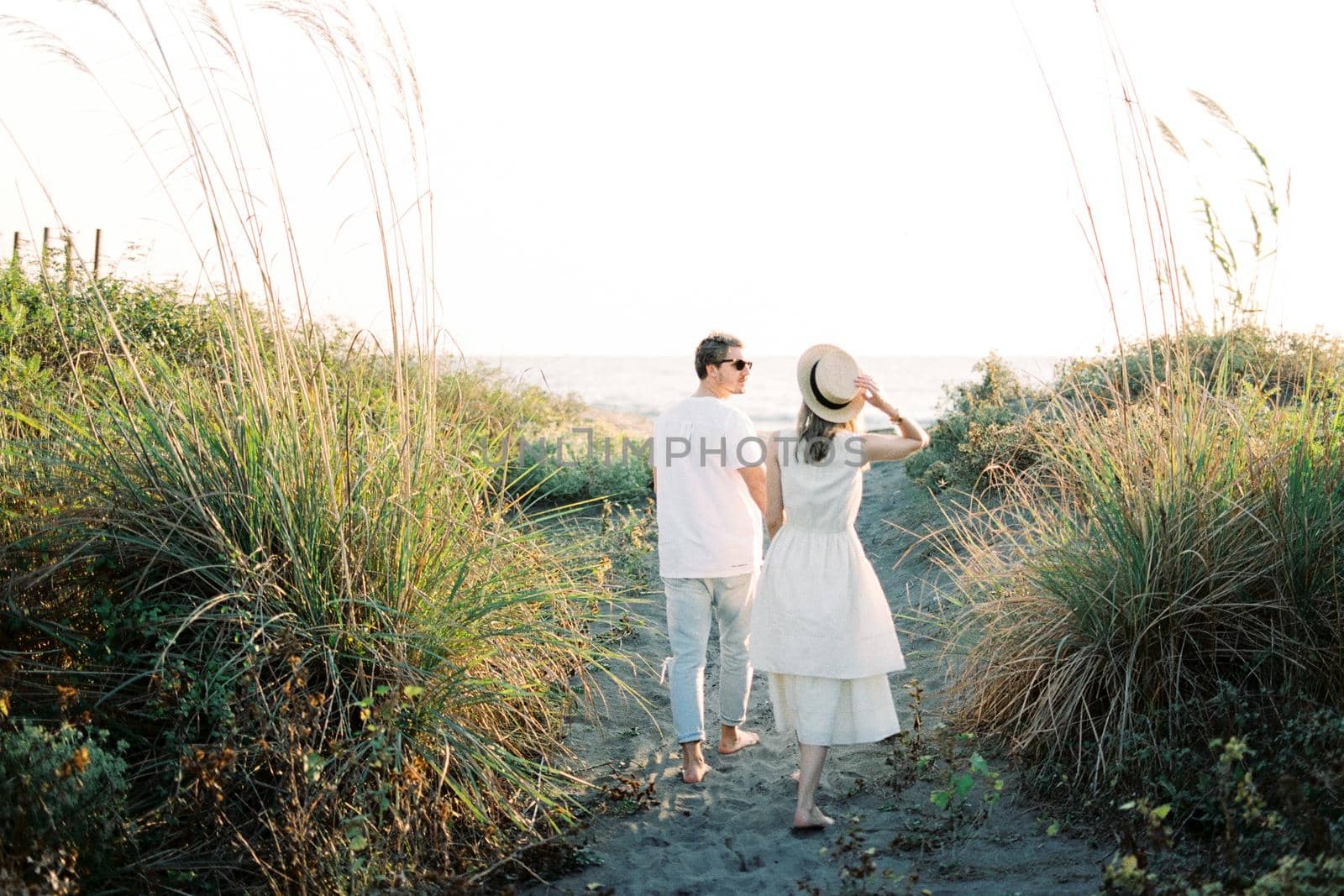Woman in a straw hat walks beside a man on a country road. Back view. High quality photo