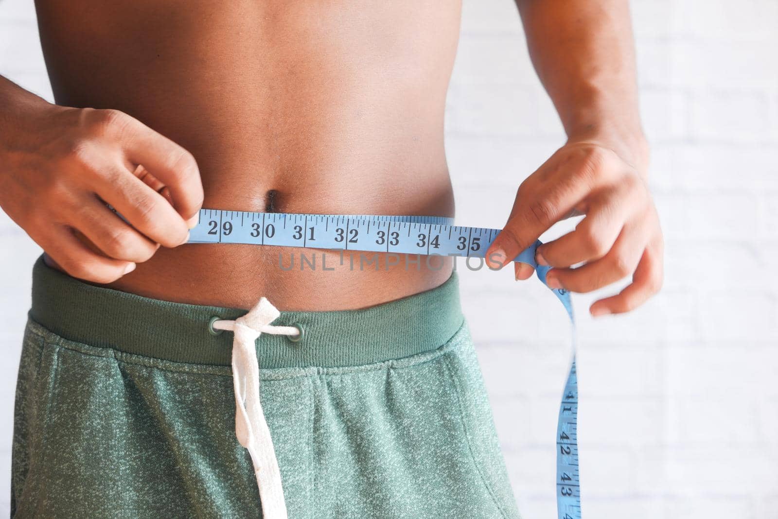 young man measuring his waist with a tape measure, close up