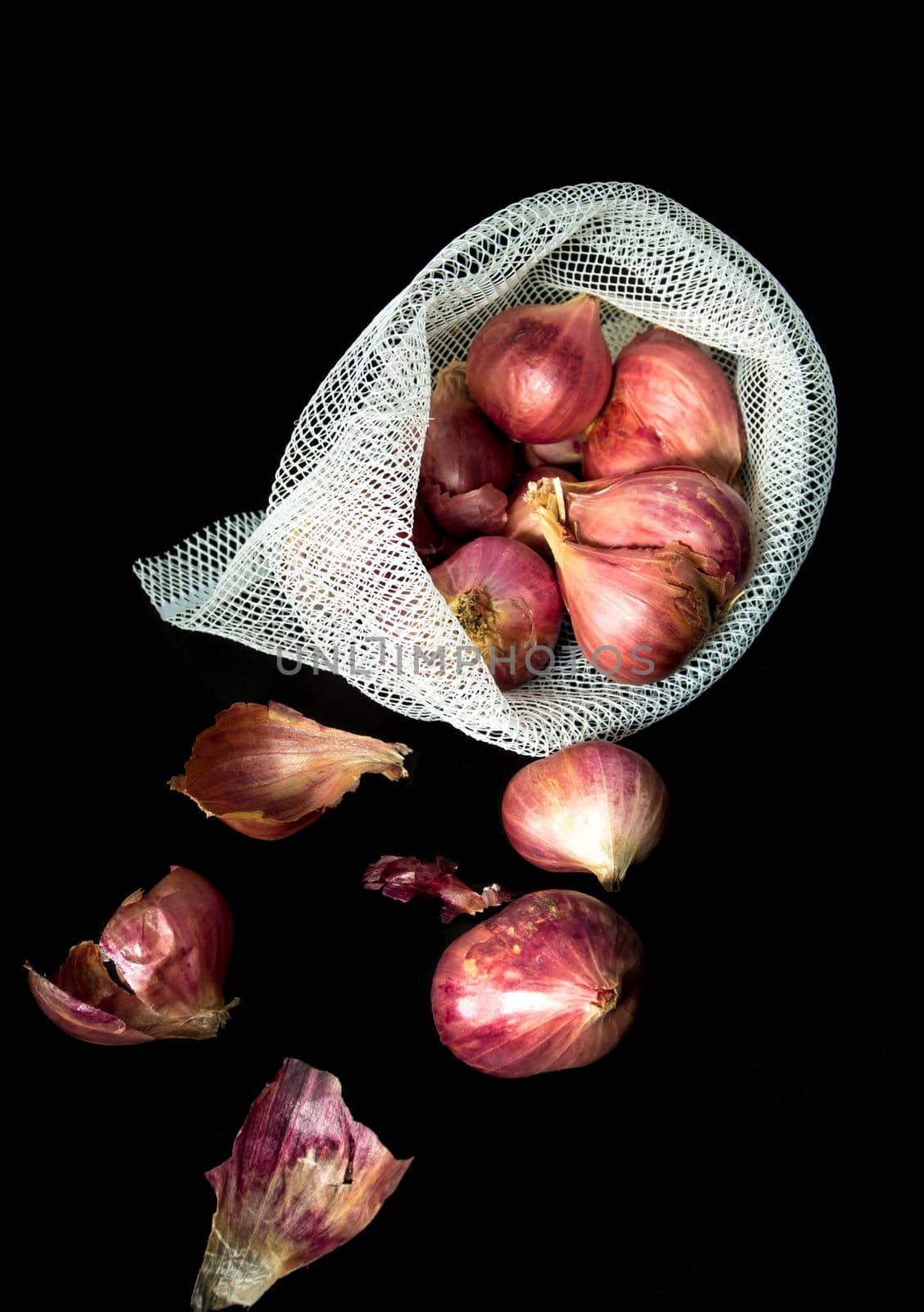 Red onions in mesh bag and some on floor isolated on black background