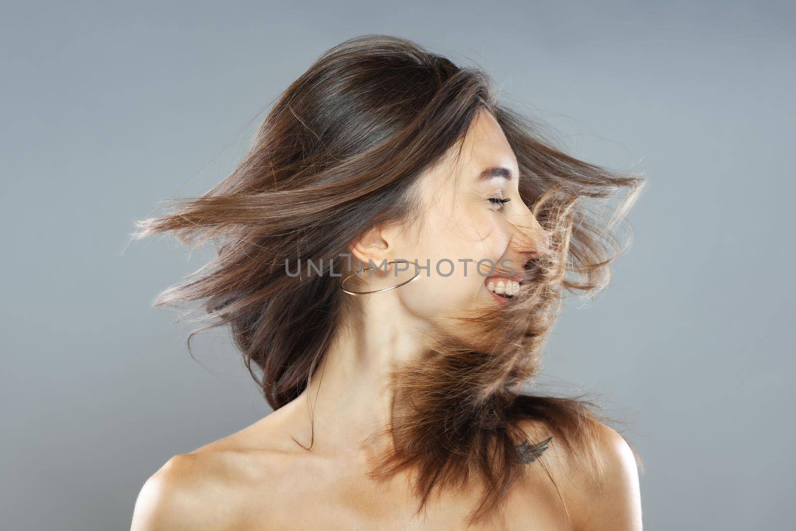 Beautiful brunette girl with hair in the air, studio portrait. Happy smiling face expression. by kokimk