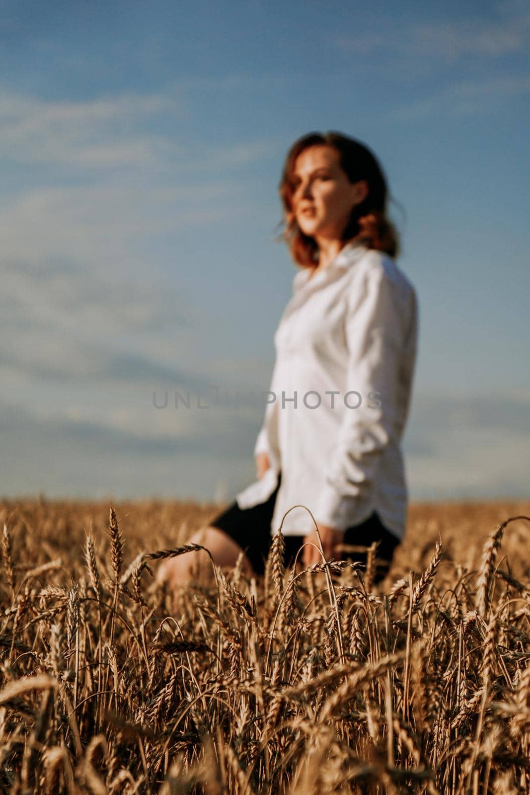 Happy young woman in a white shirt in a wheat field. Sunny day. The girl walks across the field. Blurred background, focus to foreground