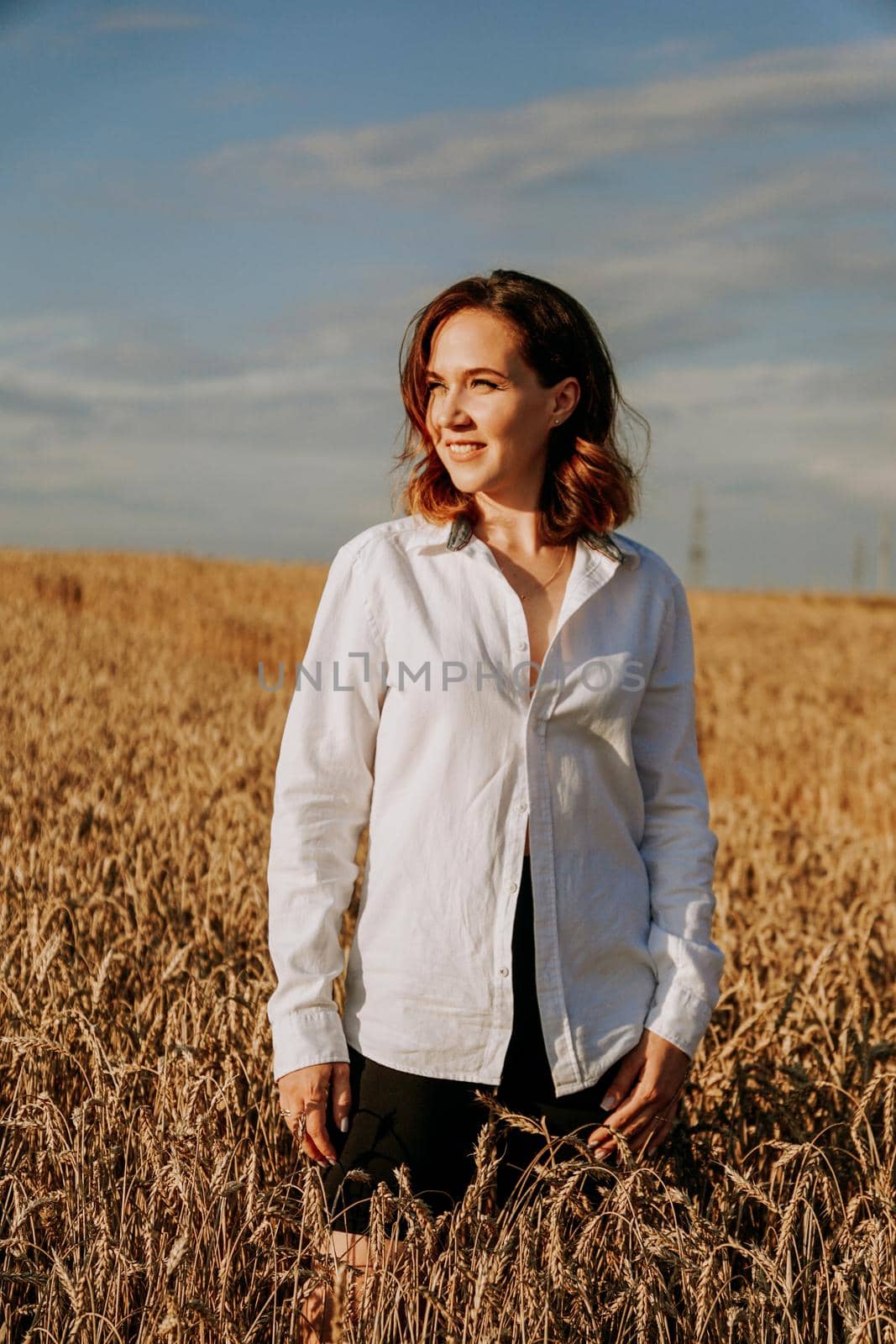 Happy young woman in a white shirt in a wheat field. Sunny day. Girl smiling, happiness concept. Vertical photo