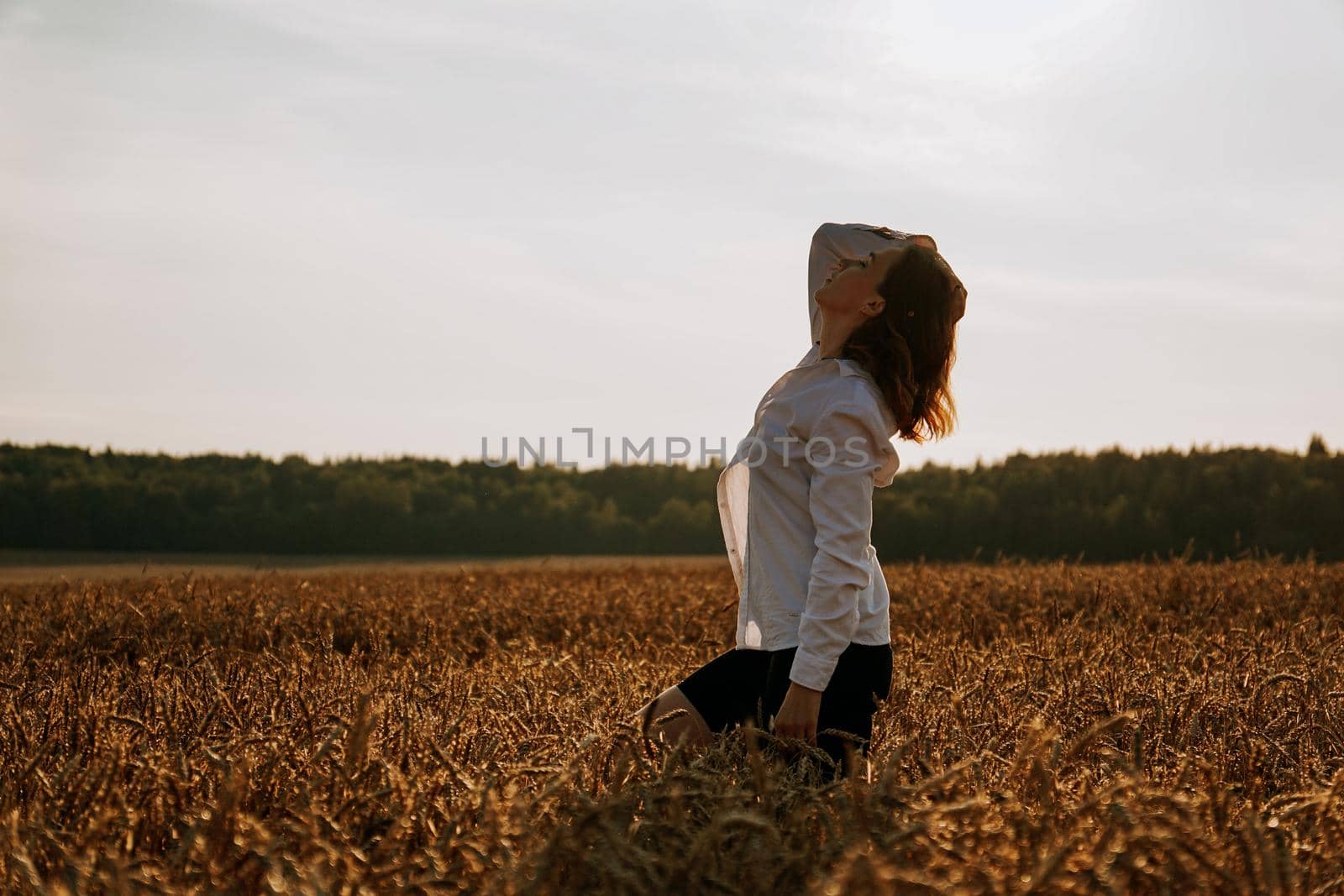 Silhouette of woman enjoying sunset. A woman in a wheat field makes flowing movements. The concept of calmness and meditation