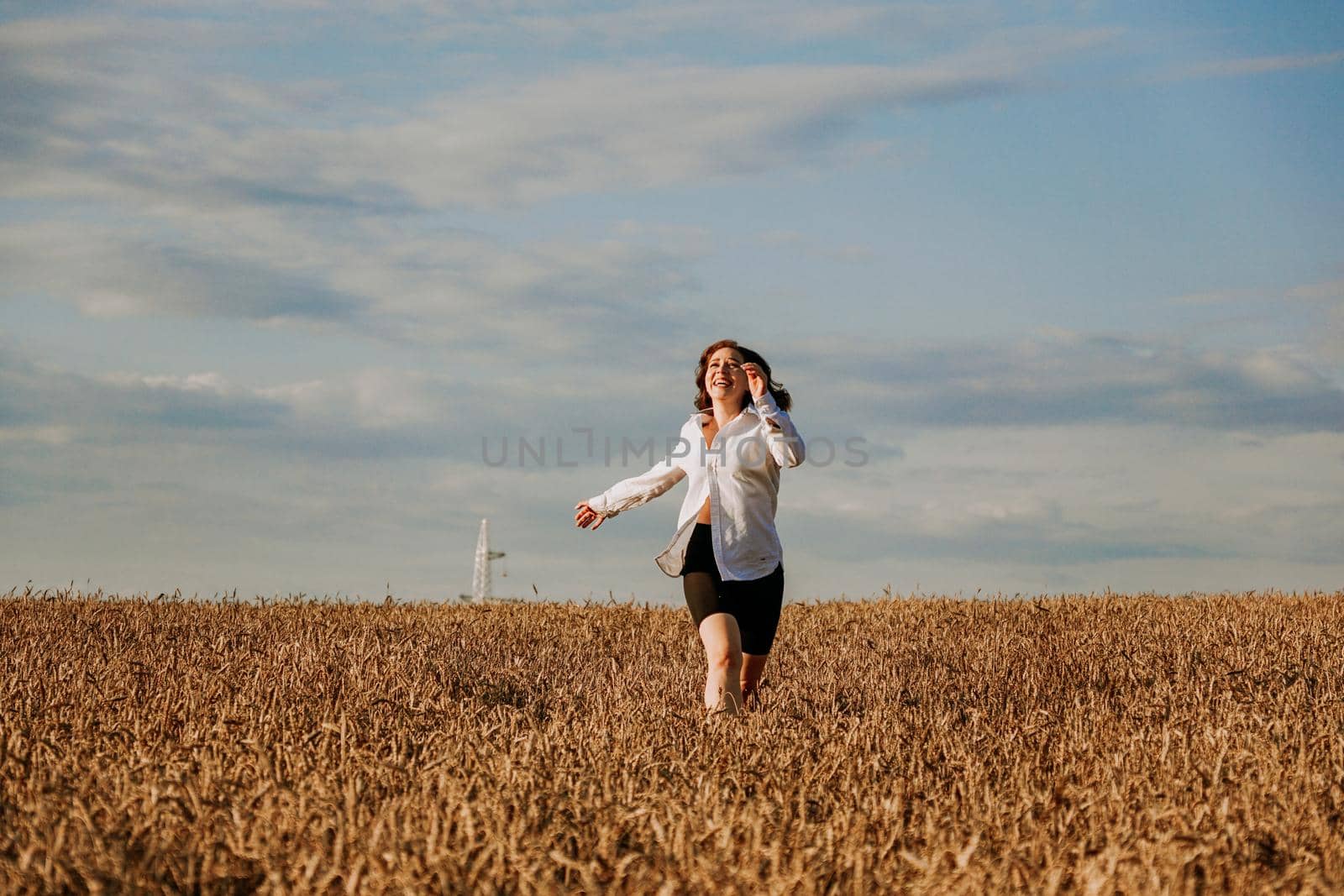 Happy woman in a white shirt runs in a wheat field on a summer day. Happiness and joy concept