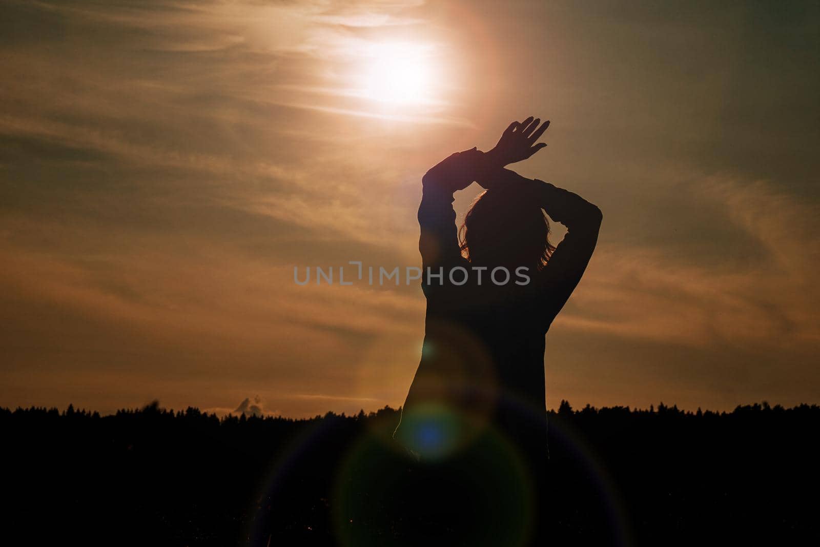 Silhouette of woman enjoying sunset. A woman in a wheat field makes flowing movements. The concept of calmness and meditation