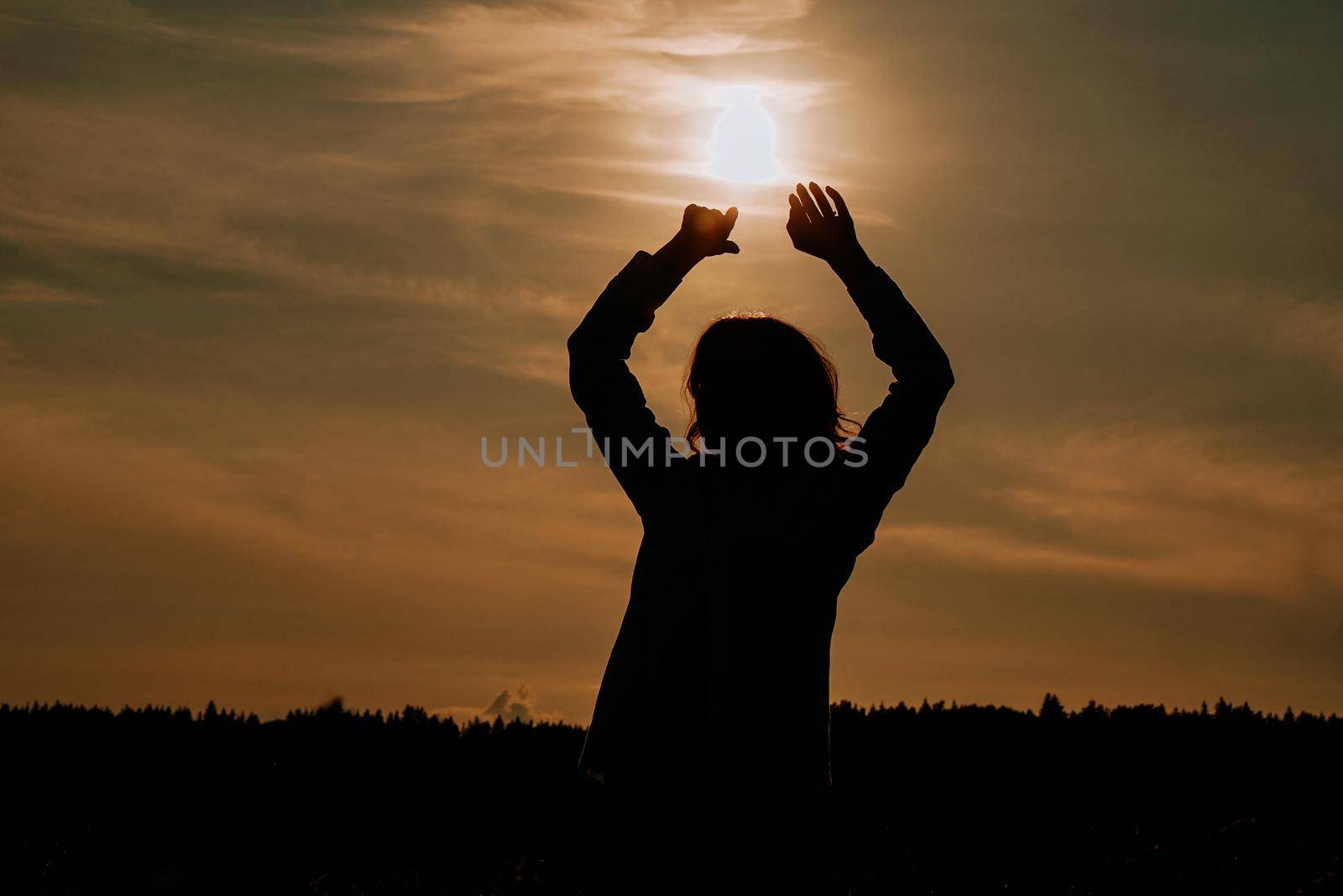 Silhouette of woman enjoying sunset. A woman in a wheat field makes flowing movements. The concept of calmness and meditation