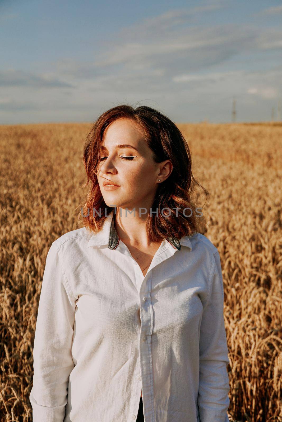 Portrait of red-haired girl in a white shirt. She in rye field on a sunny day by natali_brill