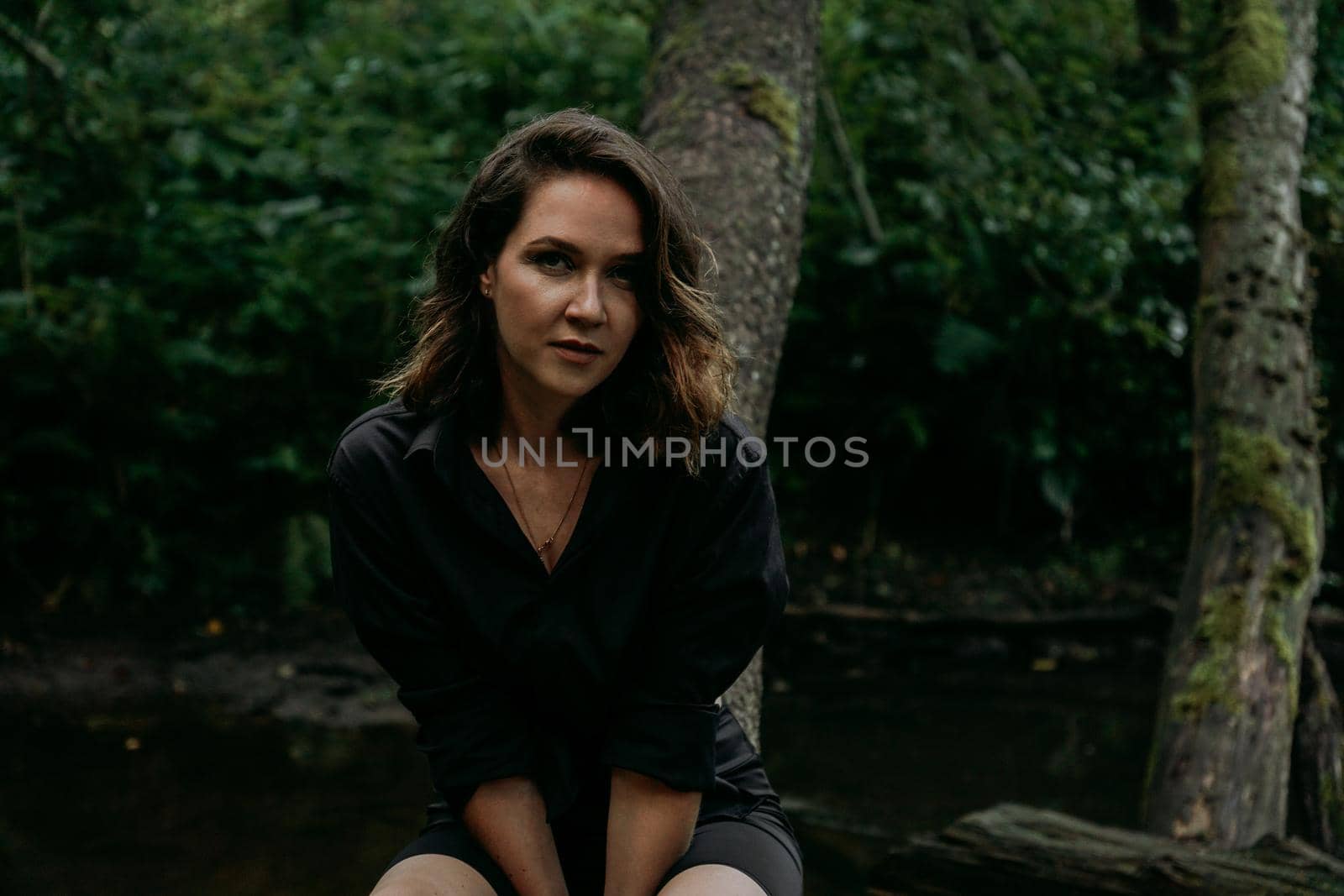 Young woman - close portrait in a dark pine forest. Woman in black shirt