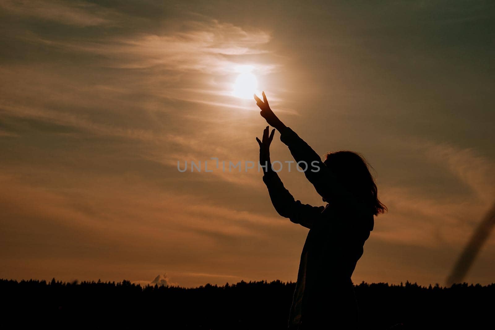 Silhouette of woman enjoying sunset. A woman in a wheat field makes flowing movements. The concept of calmness and meditation