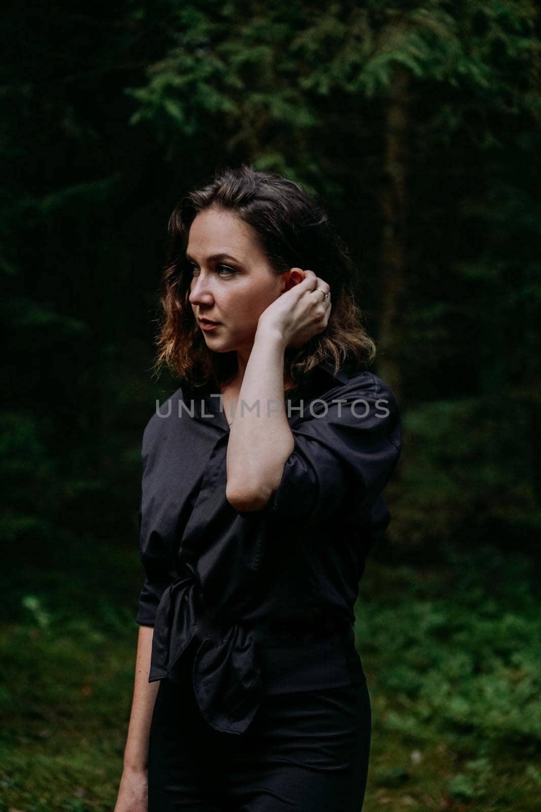 Young woman - close portrait in a dark pine forest. Woman in black shirt