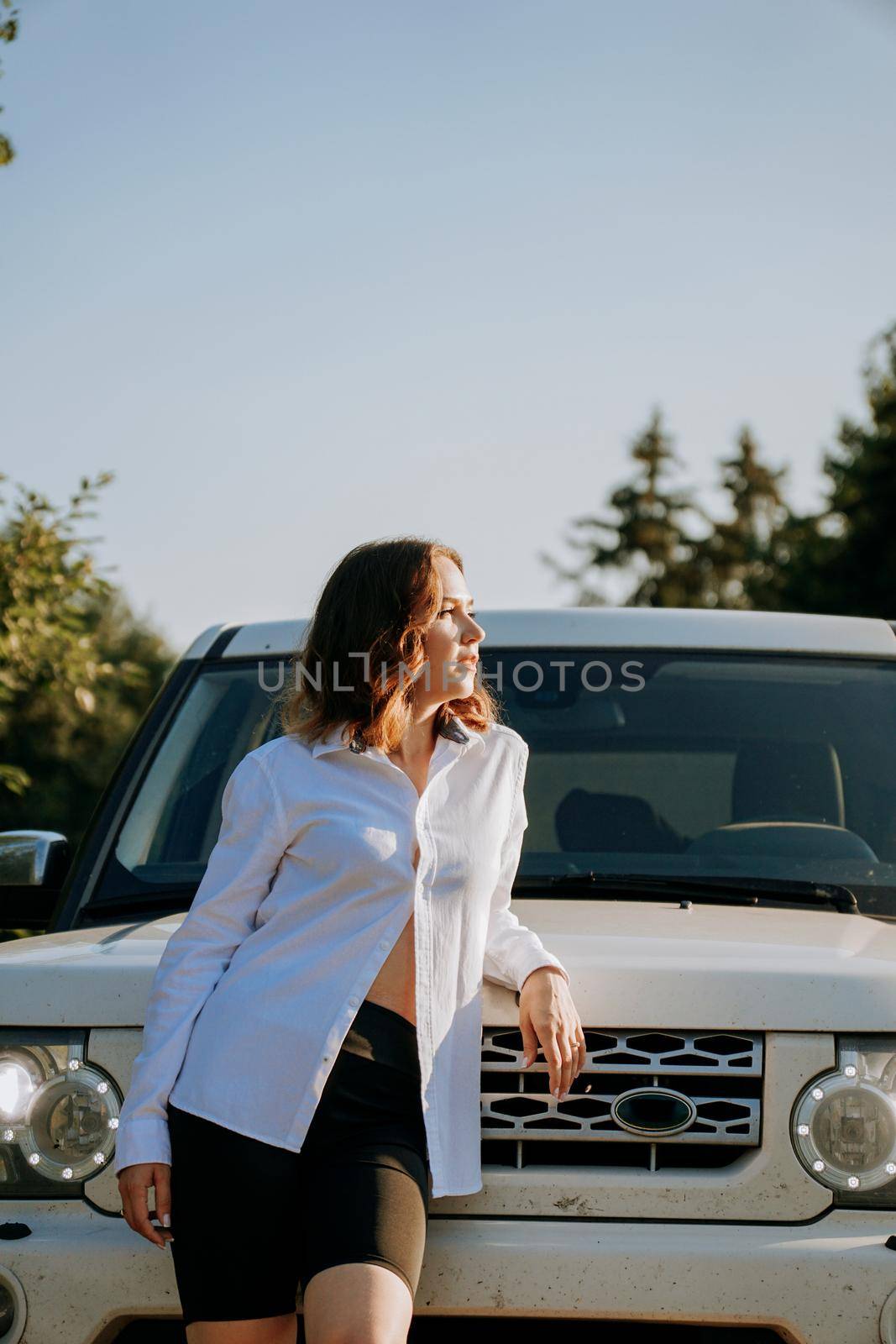 A woman in a white shirt next to a white car on the road. A trip to nature, rest outside the city. Vertical photo