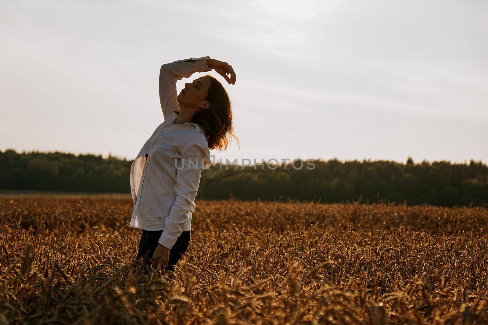 Silhouette of woman enjoying sunset. A woman in a wheat field makes flowing movements. The concept of calmness and meditation