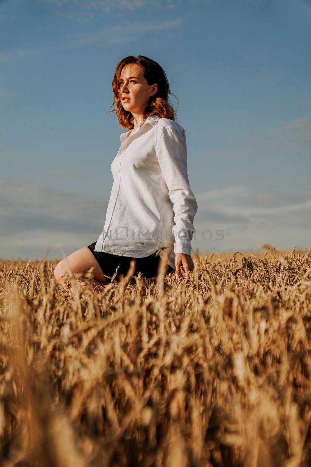 Happy young woman in a white shirt in a wheat field. Sunny day. The girl walks across the field