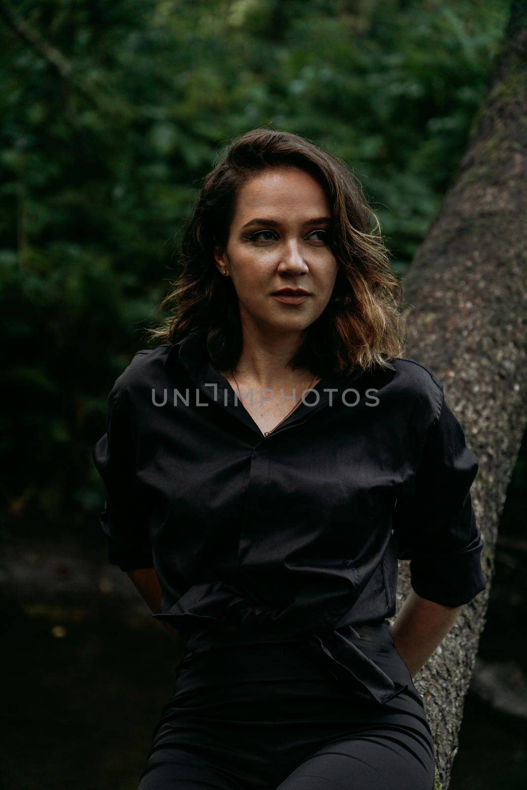 Young woman - close portrait in a dark pine forest. Woman in black shirt