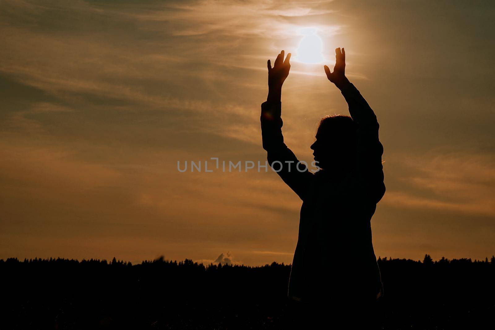 Silhouette of woman enjoying sunset. A woman in a wheat field makes flowing movements. The concept of calmness and meditation