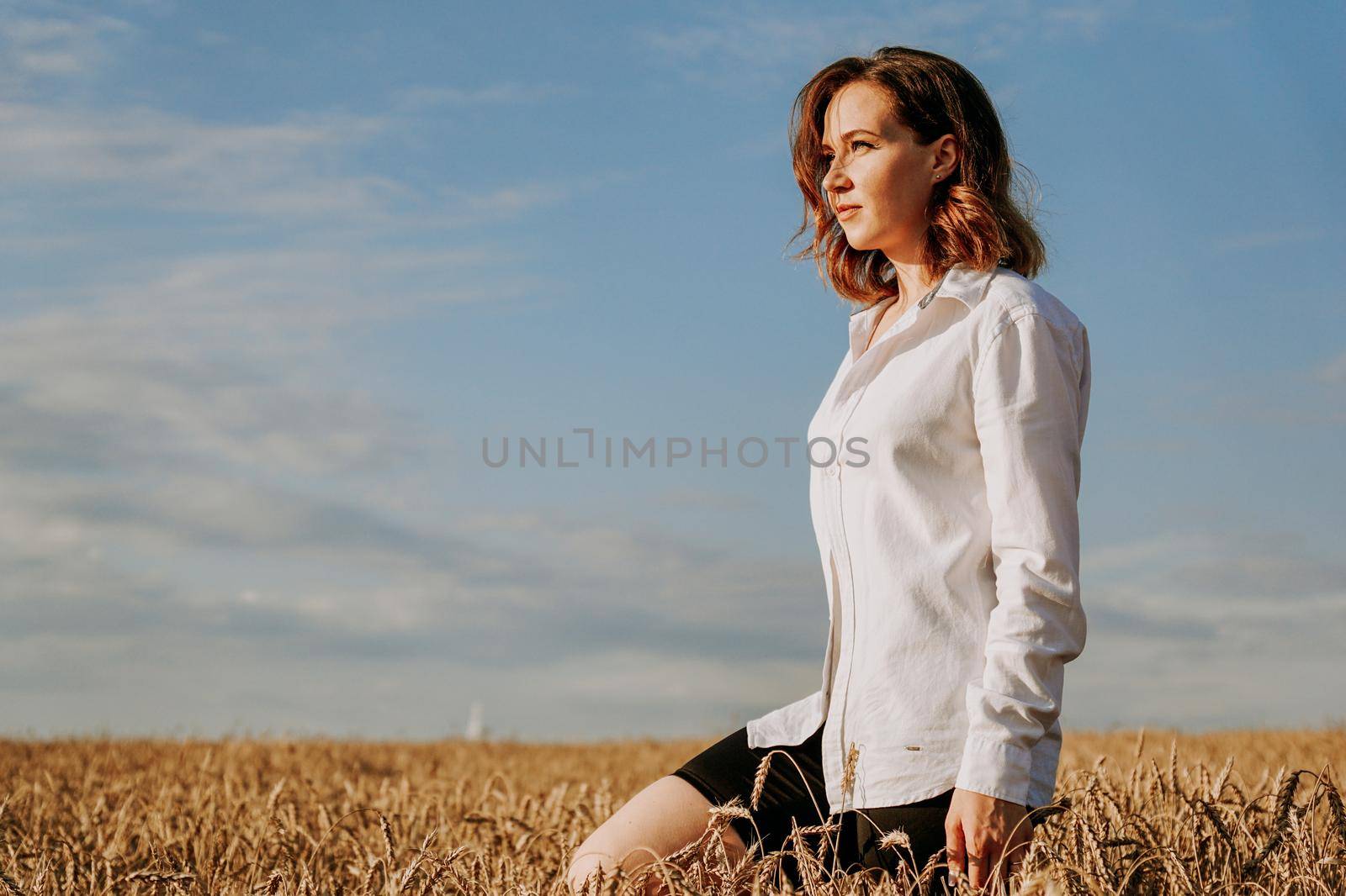 Happy young woman in a white shirt in a wheat field. Sunny day. Girl smiling, happiness concept