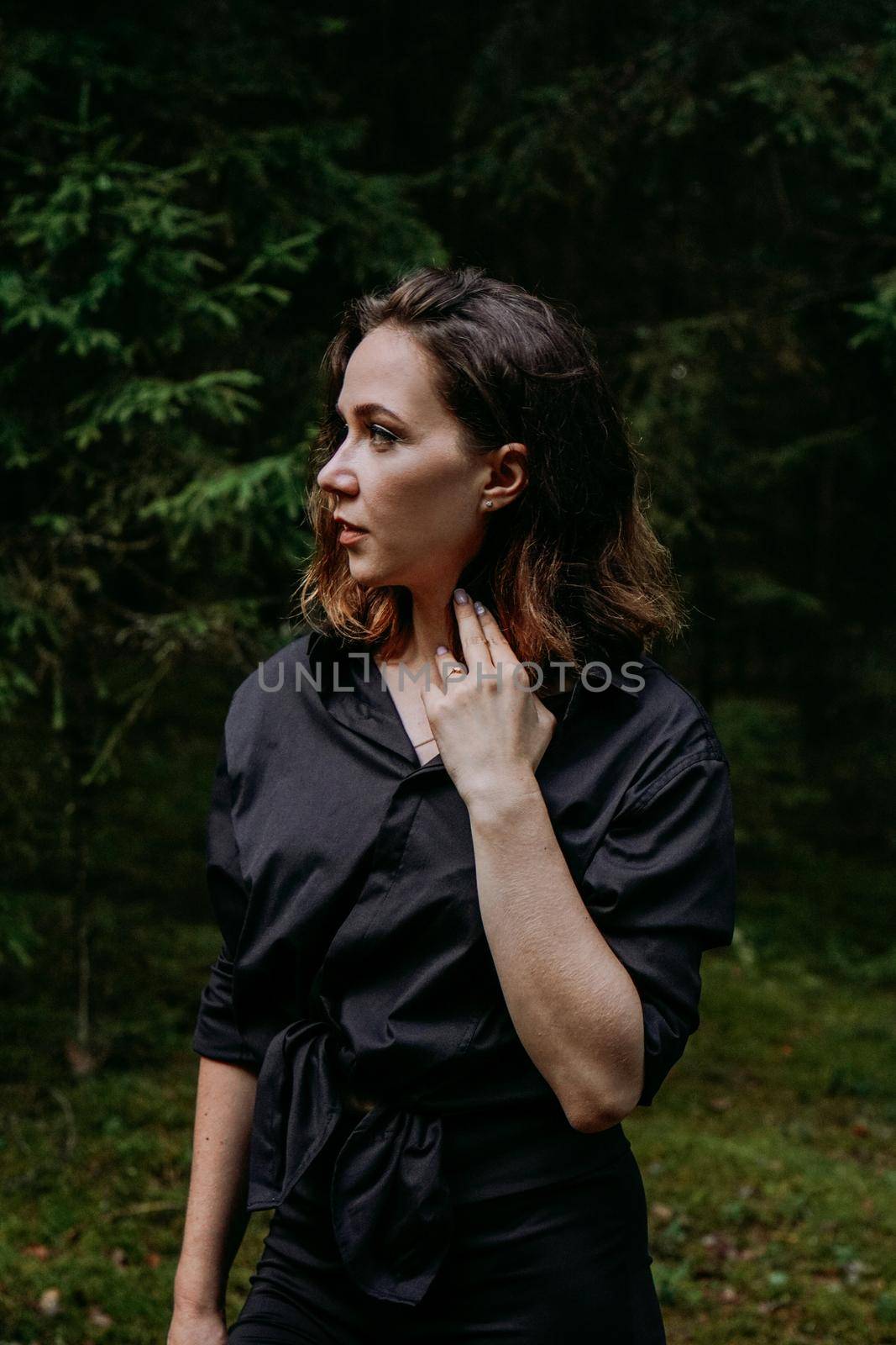 Young woman - close portrait in a dark pine forest. Woman in black shirt