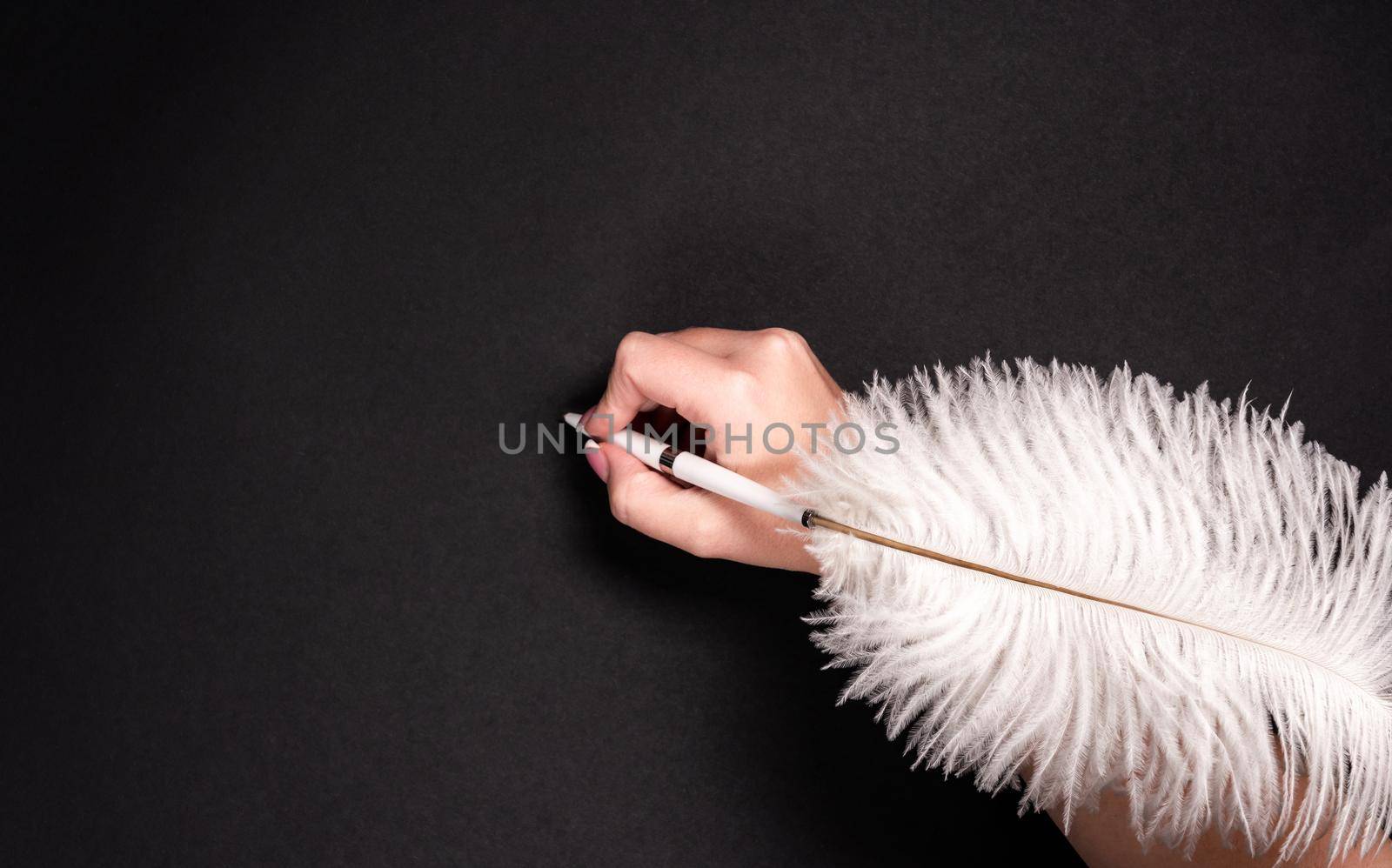 Female hand holding feather pen over black background
