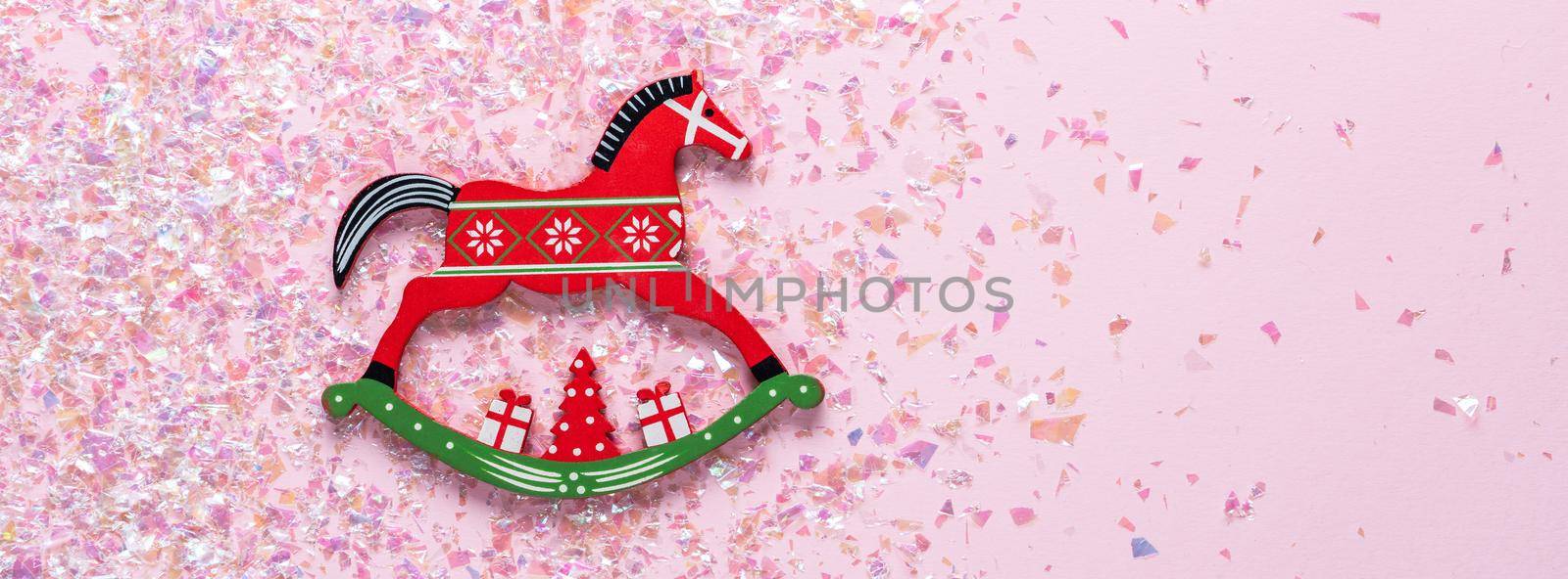 Christmas toy of rocking horse on pink background with glitter. flat lay by Mariakray