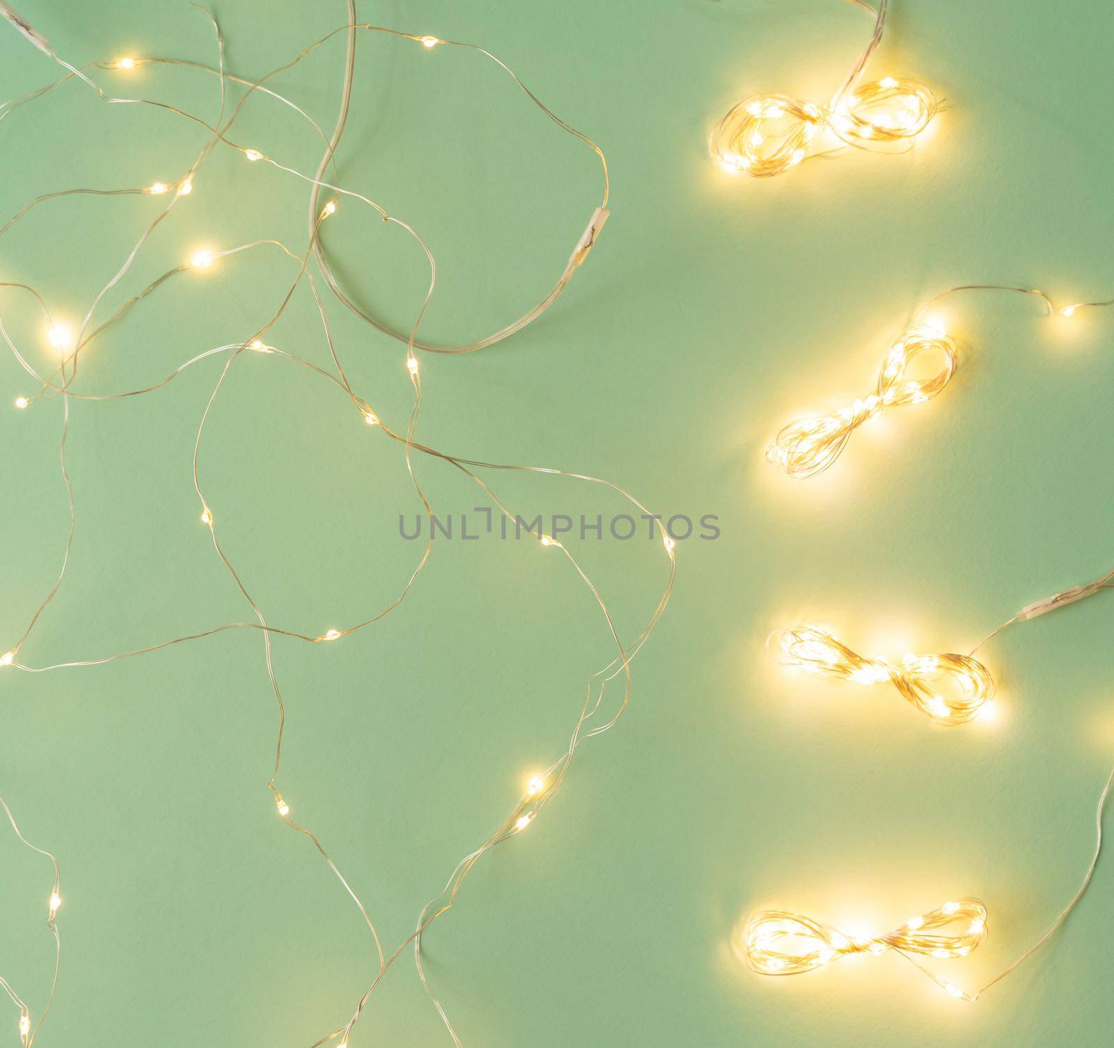 Christmas lights on light green background, flat lay with holiday garland by Mariakray