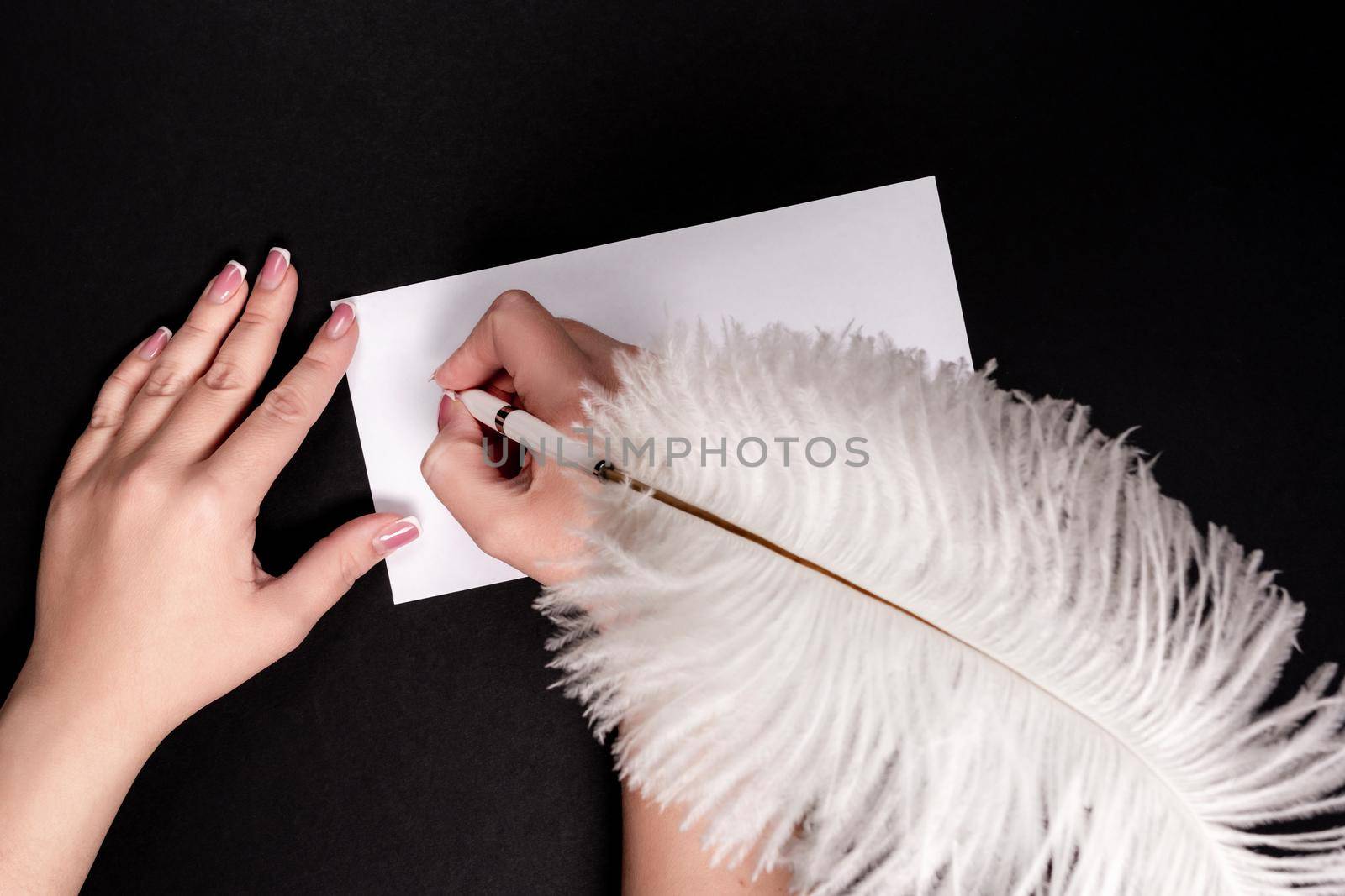 Female hands writing on white paper with feather vitage pen with copy space by Mariakray