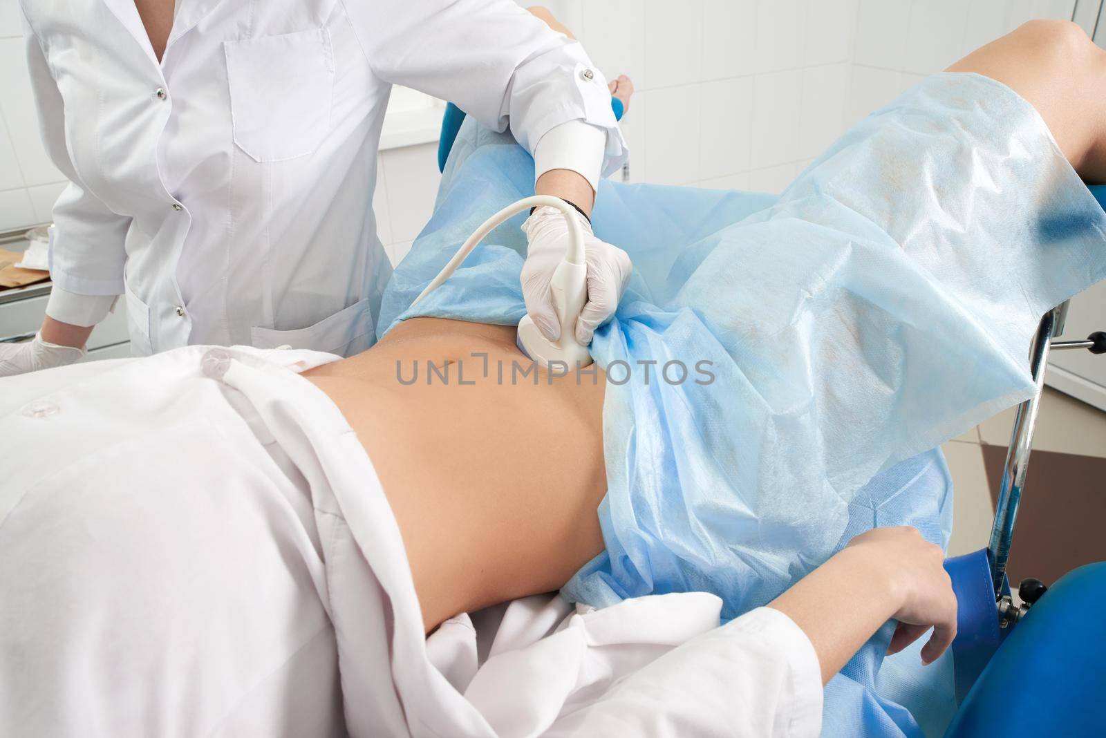 female doctor operating ultrasound scanner examining belly of her female patient by Mariakray