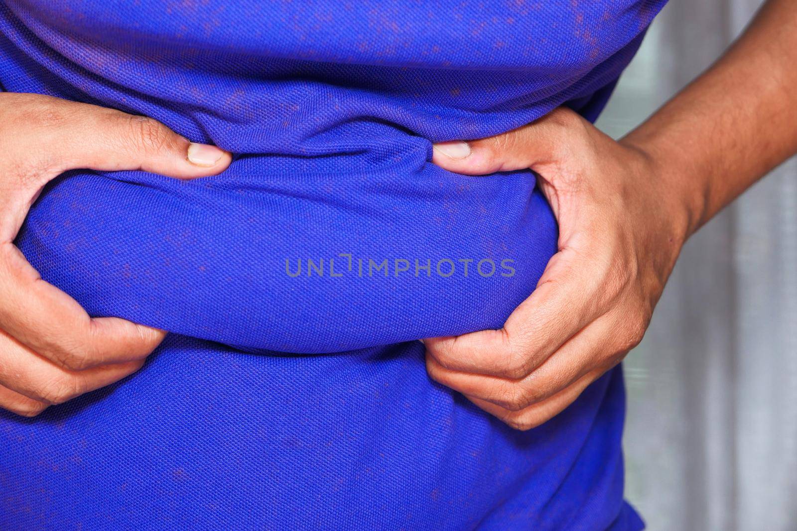 man's hand holding excessive belly fat, overweight concept.