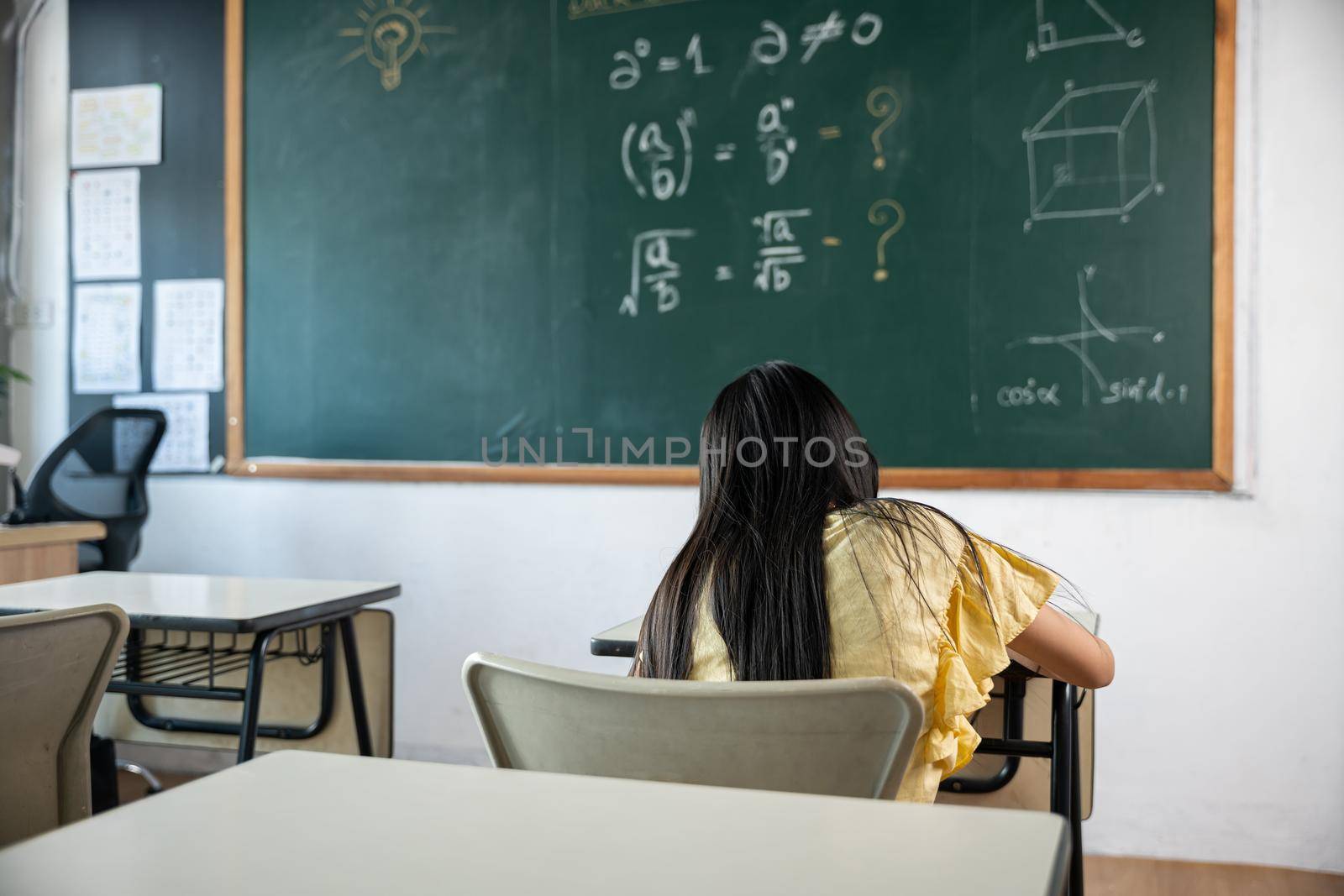 Education. Back view of school girl on lesson in classroom write hardworking on blackboard, primary child is sitting lessons at table in school writing or drawing in notebook, Back to school concept