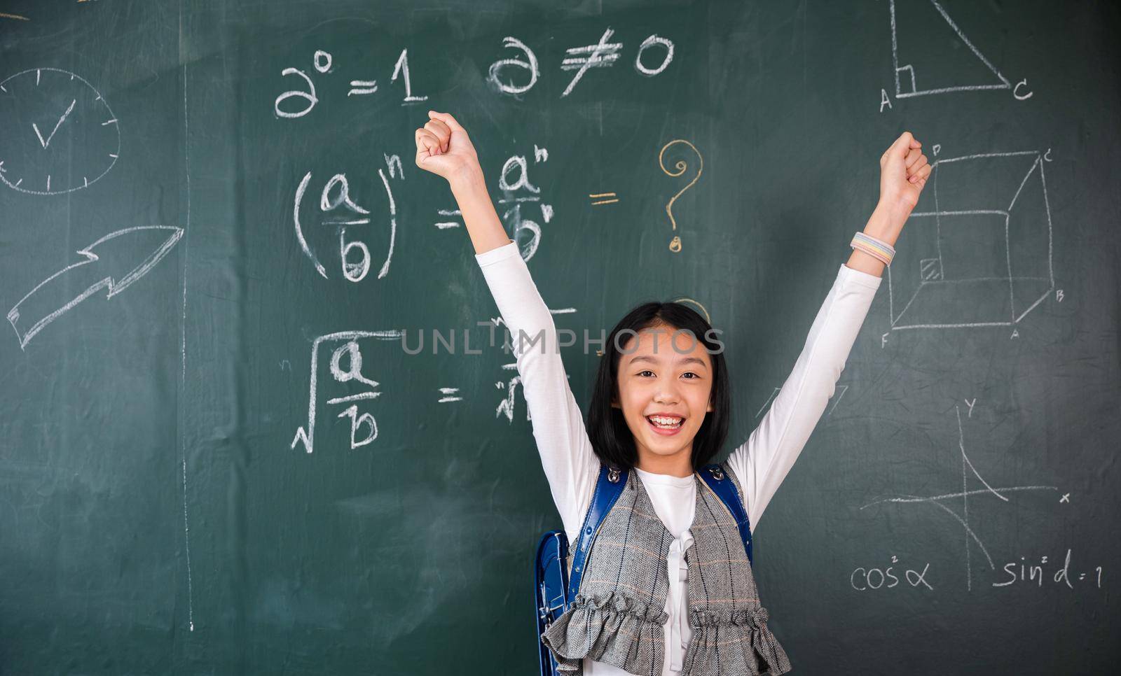Education Back to school. Asian school girl in uniform on classroom raised arms to successful finished homework, primary child is standing front of class in school raised hands in win position