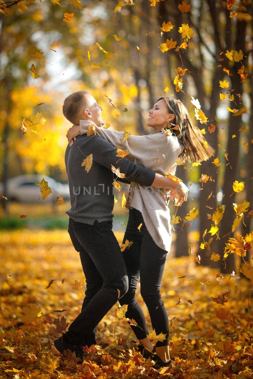 Young couple in love whirl in dance on dating in autumn nature under autumn leaf fall.