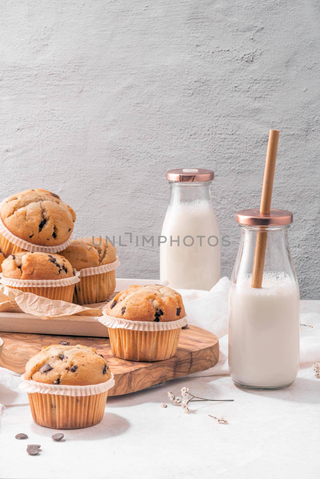 Chocolate chip muffins with milk served on glass bottles on white kitchen countertop.