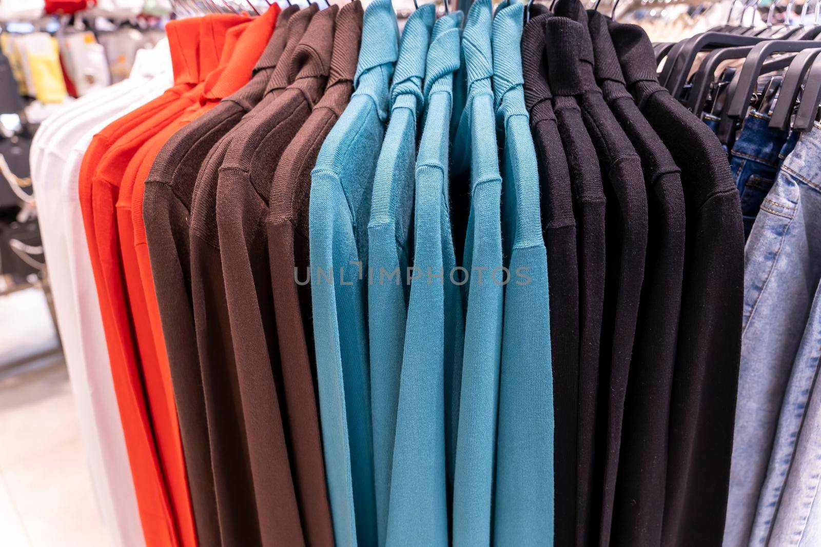 multi colored sweatshirts hang on a hanger in a clothing store. Close-up: Hangers with casual clothes in a mall. Designer clothing collection. New collection in fashion boutique