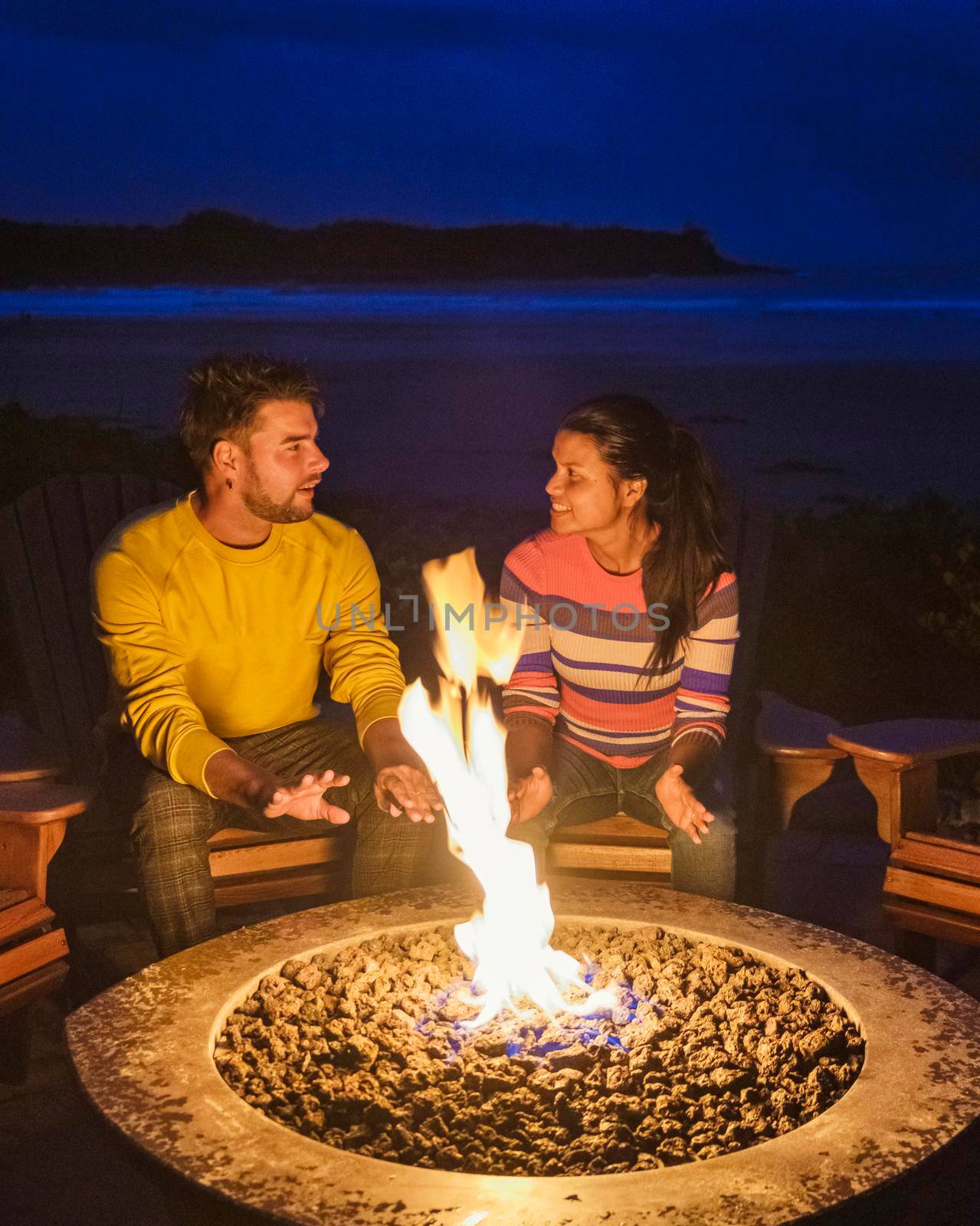 a couple of men and women mid-age by a campfire on the beach of Tofino Vancouver Island Canada,