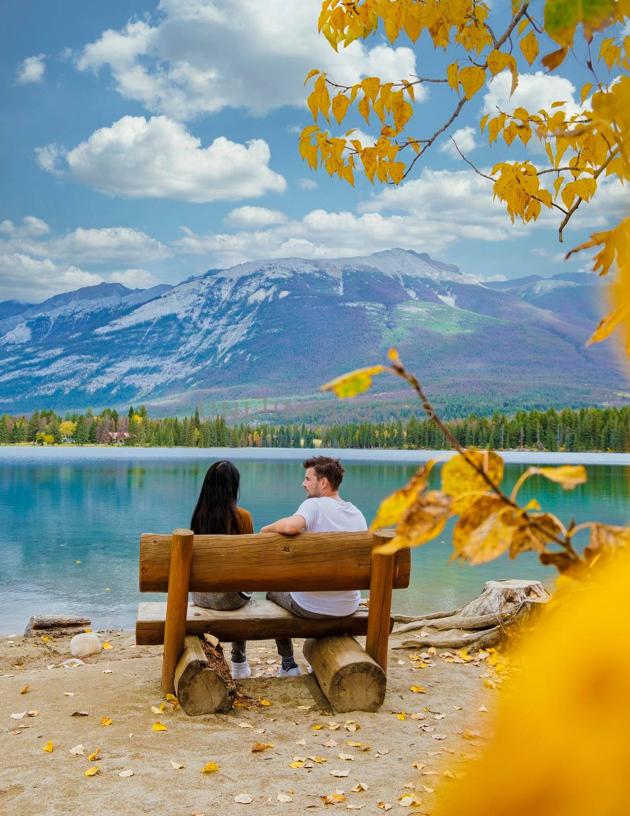Beauvert lake at Jasper with autumn trees, Canada, a Canadian lake popular for the canoe in Canada. couple men and women sitting on a bench looking out over the lake with colorful autumn trees