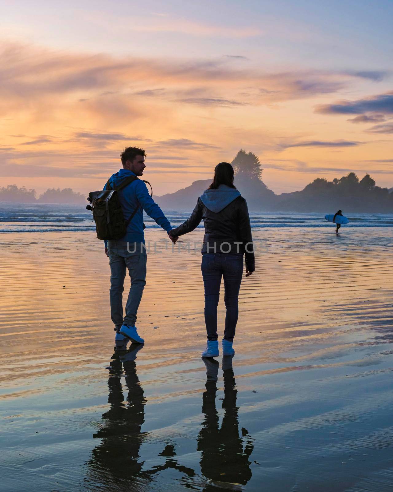 a couple of men and women mid-age watching the sunset on the beach of Tofino Vancouver Island Canada, beautiful sunset on the beach with pink-purple colors in the sky. Canada Tofino Vancouver Island