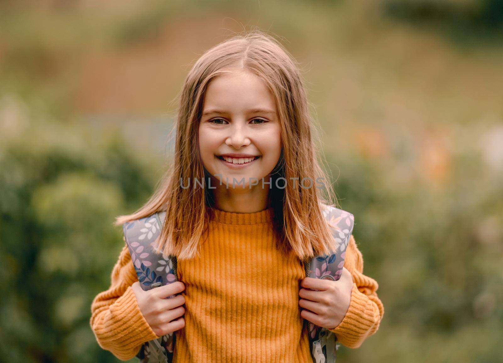 Pretty school girl with backpack looking at camera and smiling. Carefree child kid at autumn outdoors portrait