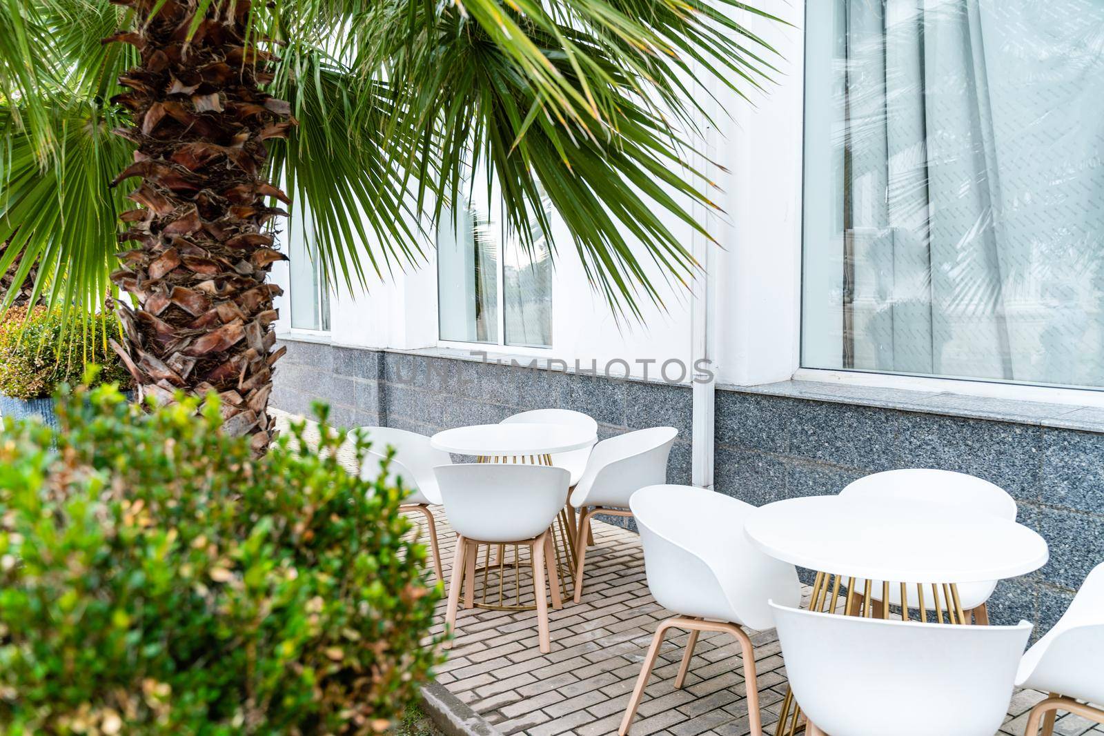 Street cafe with white chairs, green foliage around. Without people, tourism, travel