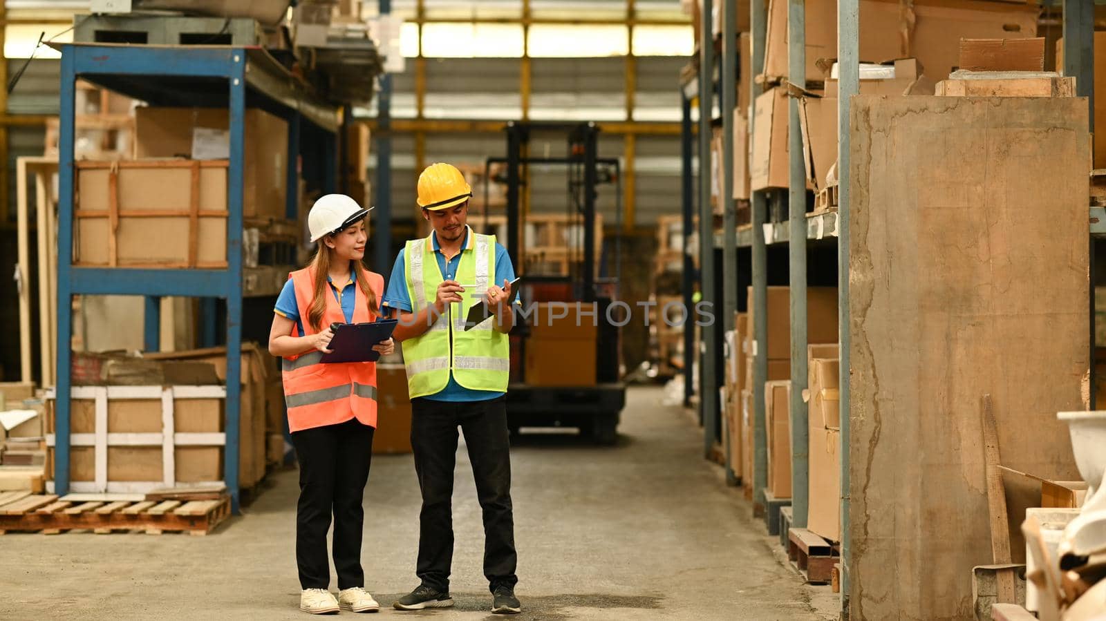 Full length of female managers and worker checking inventory in a warehouse with shelves full of cardboard boxes in the background.