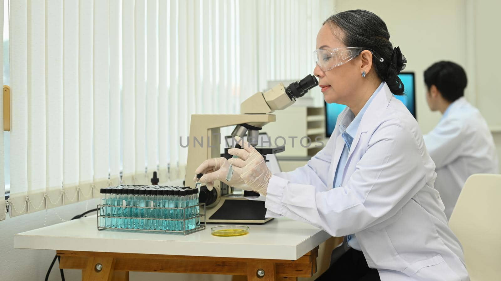Mature female scientist in white coat examining samples and liquid in laboratory. Medicine and science researching concepts.
