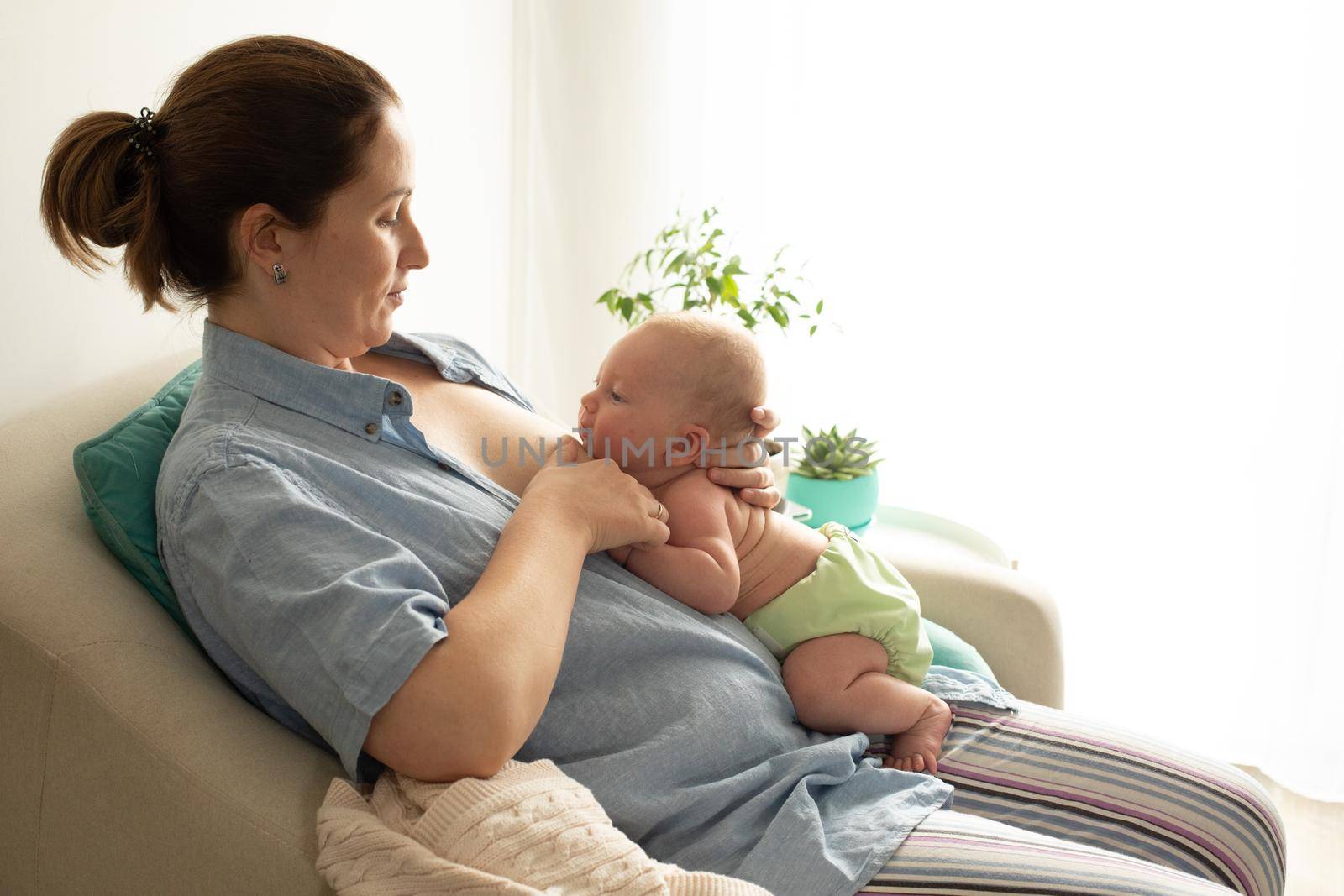 Breastfeeding in laid back position. Mothed and baby at the chair.