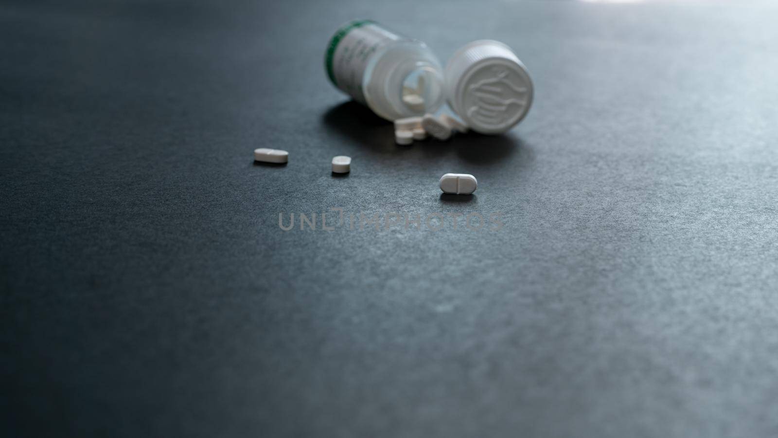 White tablets pills and blur plastic pill bottle on dark floor. Prescription drugs. Pharmaceutical industry. Medical care. Medication for cure illness. Pharmacy. Small white pills. Dose recommended.