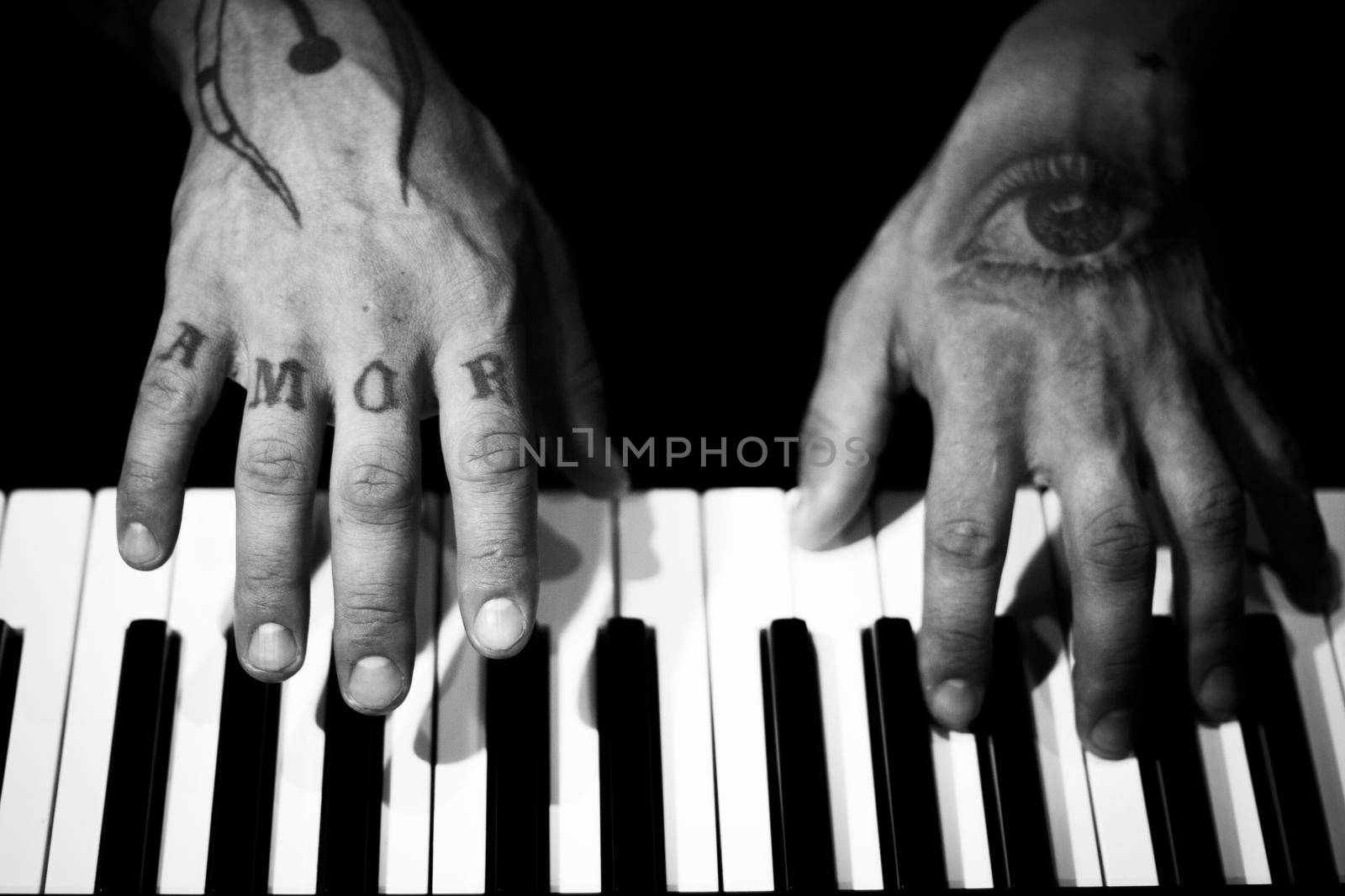 Tattooed mans hands on the keyboard of a piano. Dark background