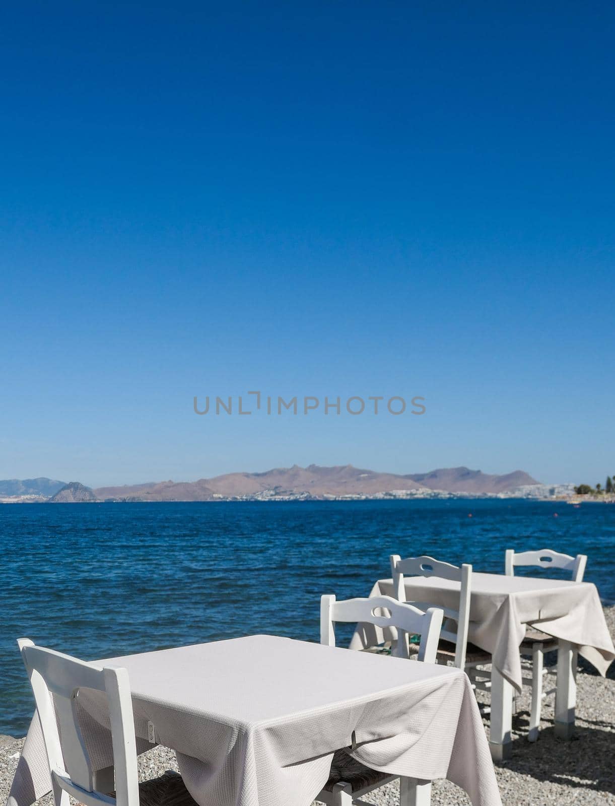 White restaurant tables on the beach in summer - travel, vacation and summer concept. The perfect lunch with a sea view